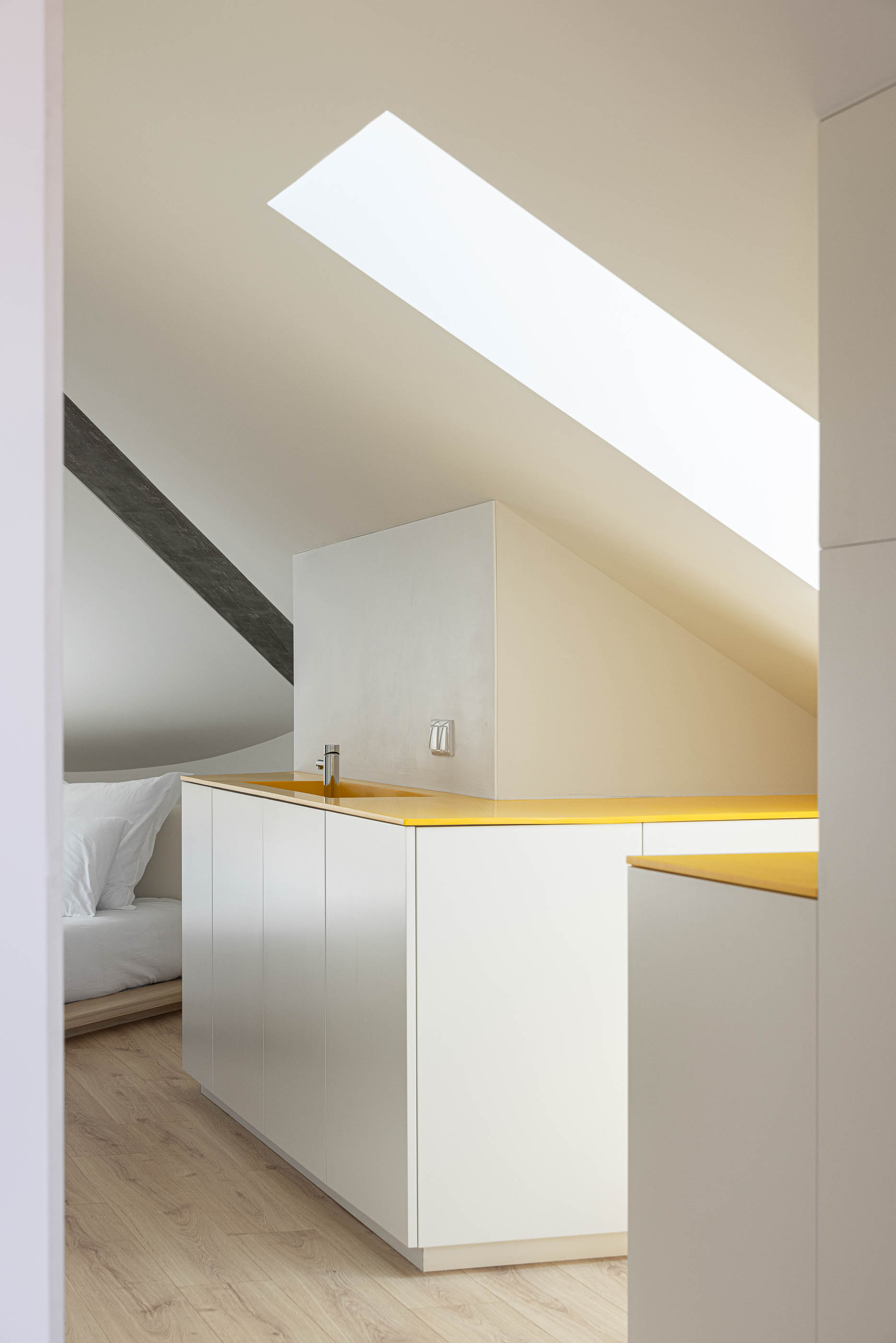 Quarto: Interior com kitchenette branca e amarela, teto inclinado e pavimento em madeira clara. — A'mar arquitetura REM'A Arquitectos em Póvoa de Varzim
