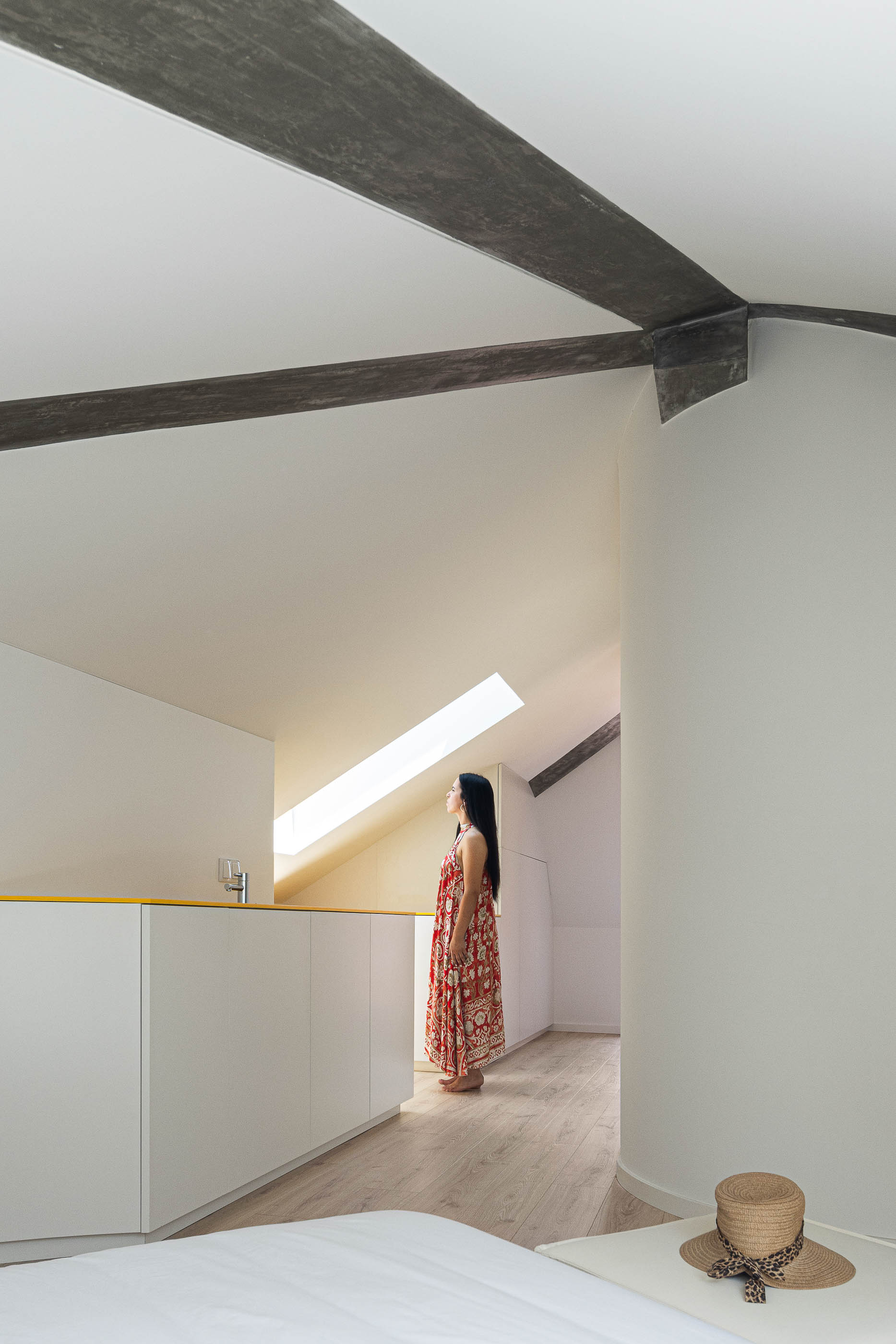 Quarto: Interior com kitchenette branca e amarela, teto inclinado com vigas em betão e pavimento em madeira. — A'mar arquitetura REM'A Arquitectos em Póvoa de Varzim