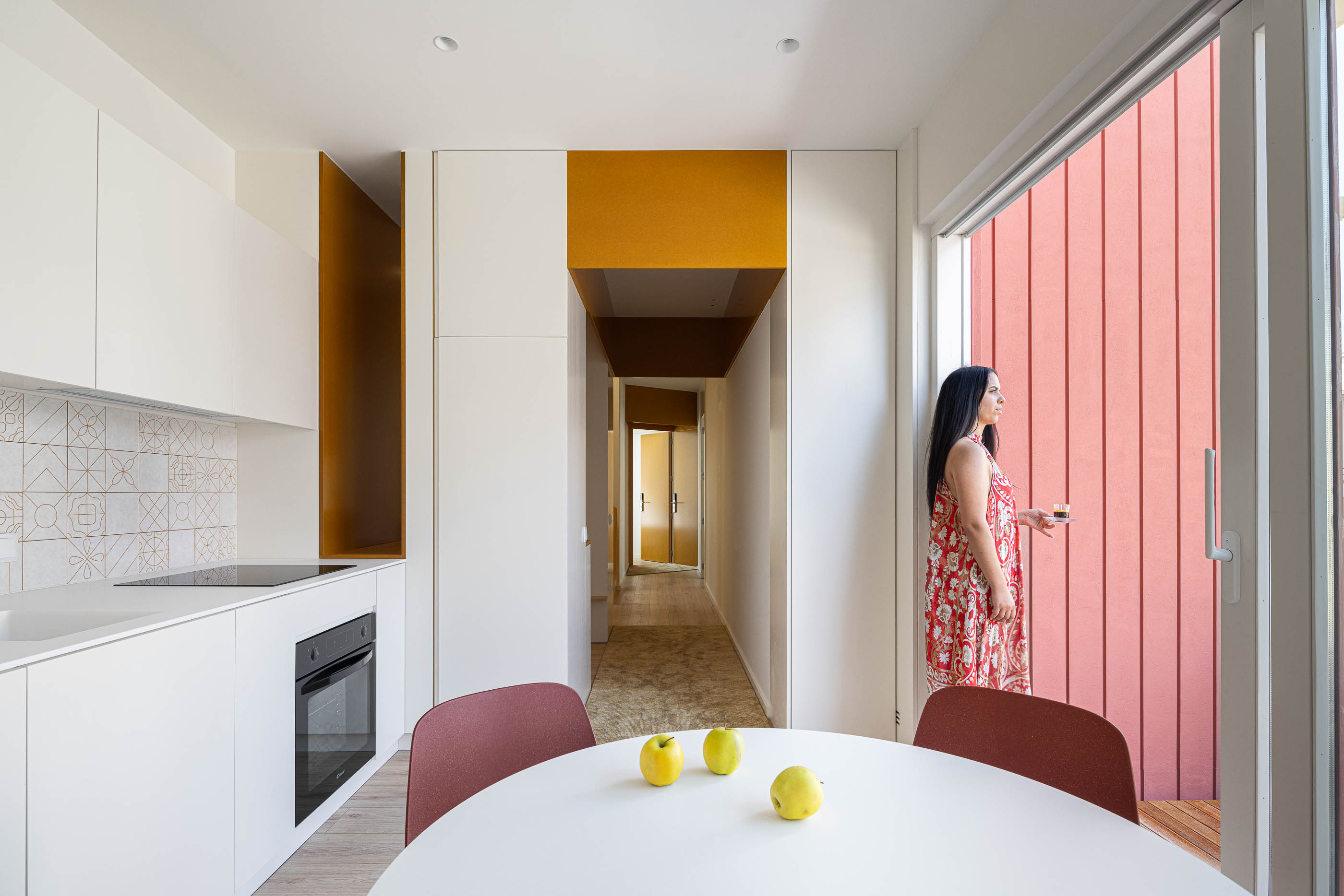 Cozinha: Interior com armários brancos, mesa redonda, cadeiras vermelhas e porta de correr para o exterior. — A'mar arquitetura REM'A Arquitectos em Póvoa de Varzim