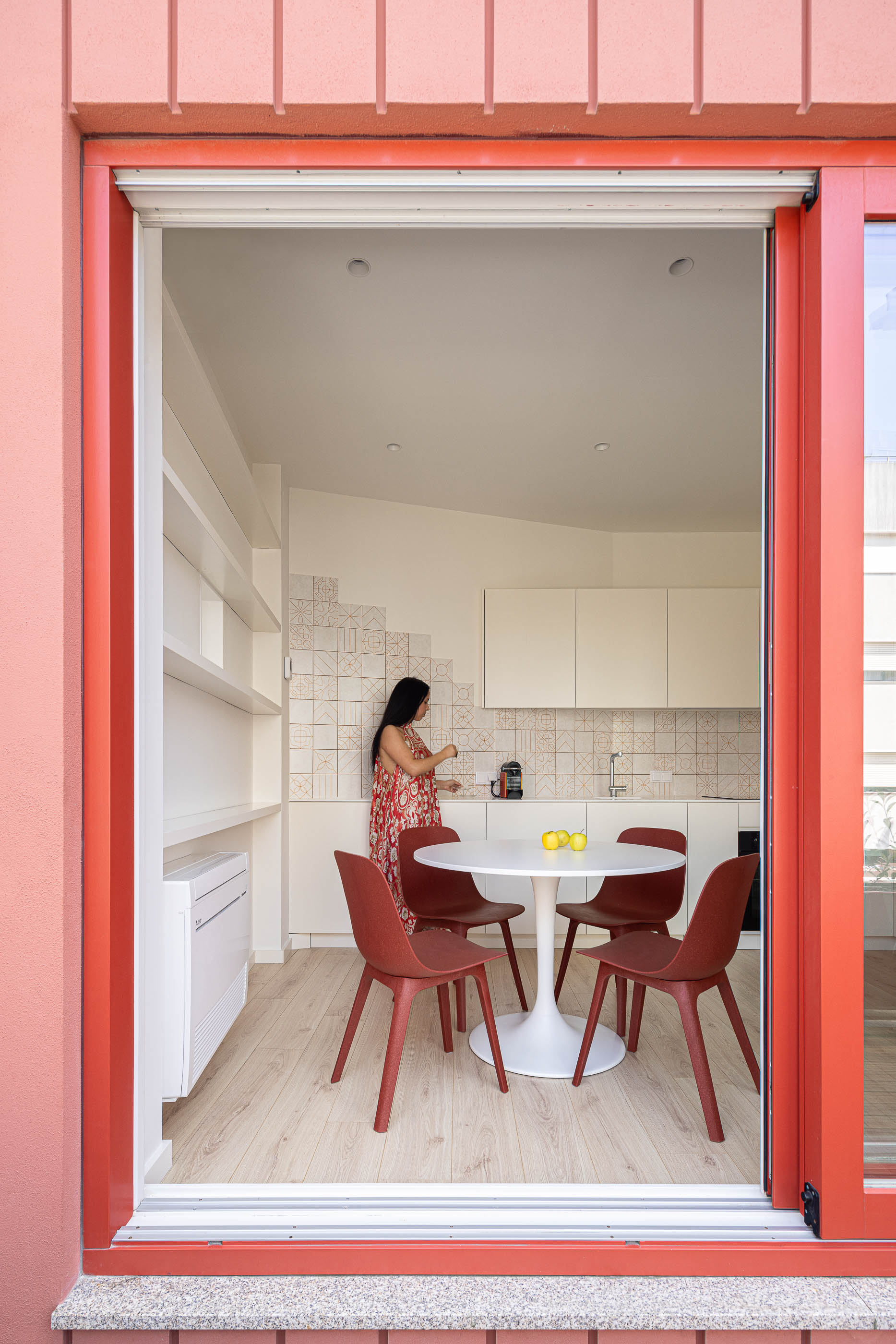 Cozinha: Interior com mesa redonda, cadeiras vermelhas e armários brancos, visto do exterior. — A'mar arquitetura REM'A Arquitectos em Póvoa de Varzim