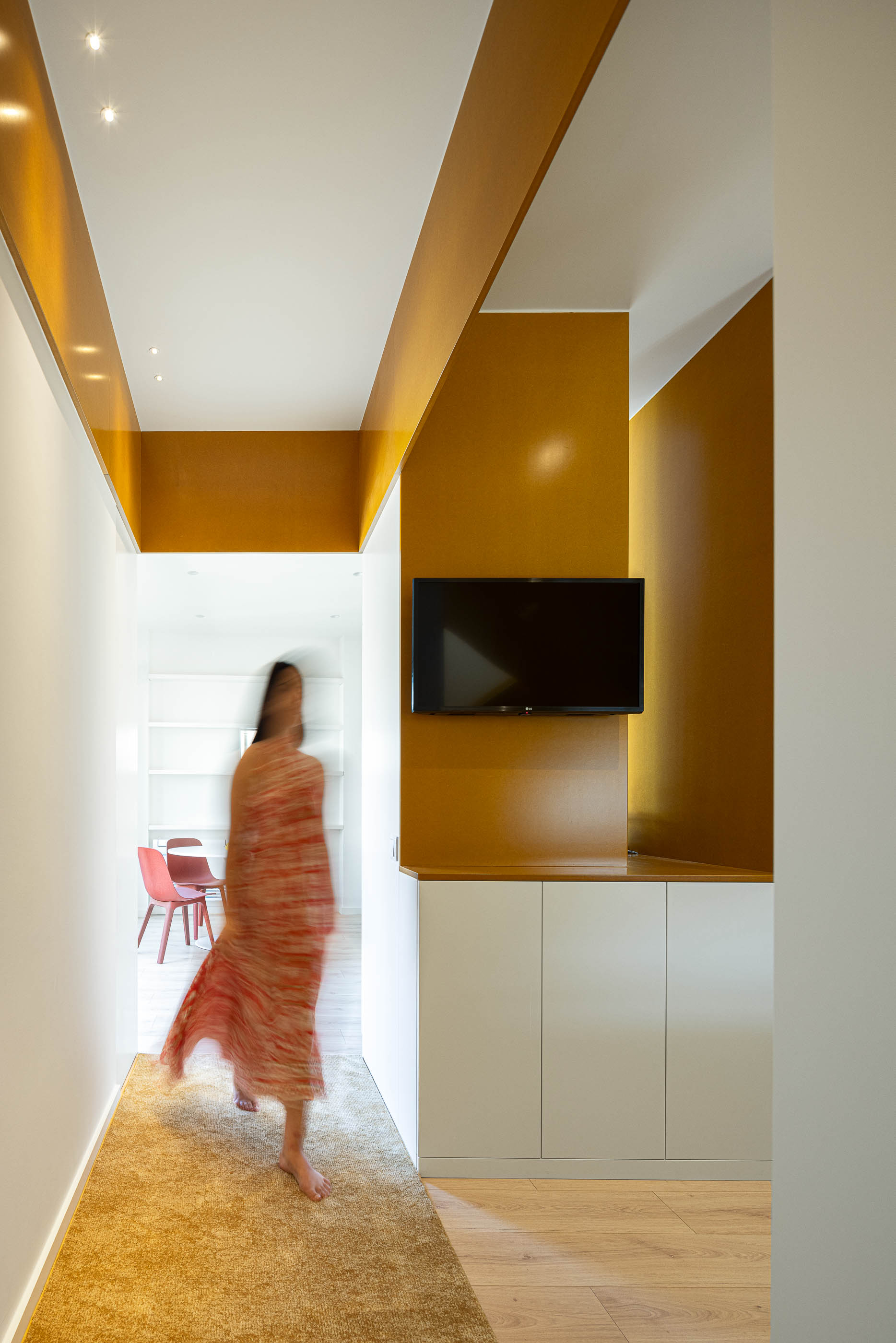 Corredor: Corredor com alcatifa, armários brancos, detalhes em amarelo e televisão na parede. — A'mar arquitetura REM'A Arquitectos em Póvoa de Varzim