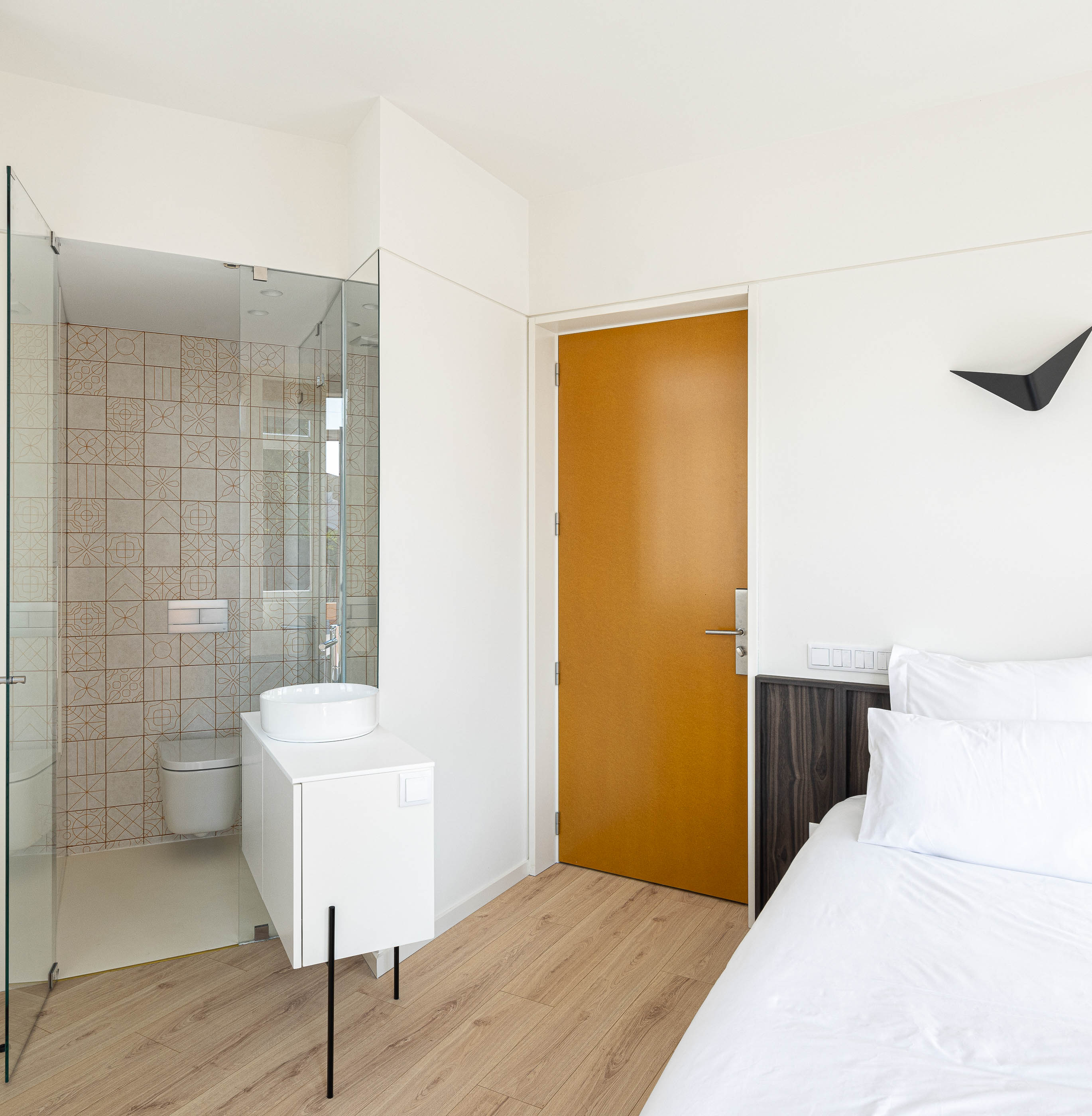 Quarto: Quarto com cama de casal, casa de banho integrada e pavimento em madeira clara. — A'mar arquitetura REM'A Arquitectos em Póvoa de Varzim