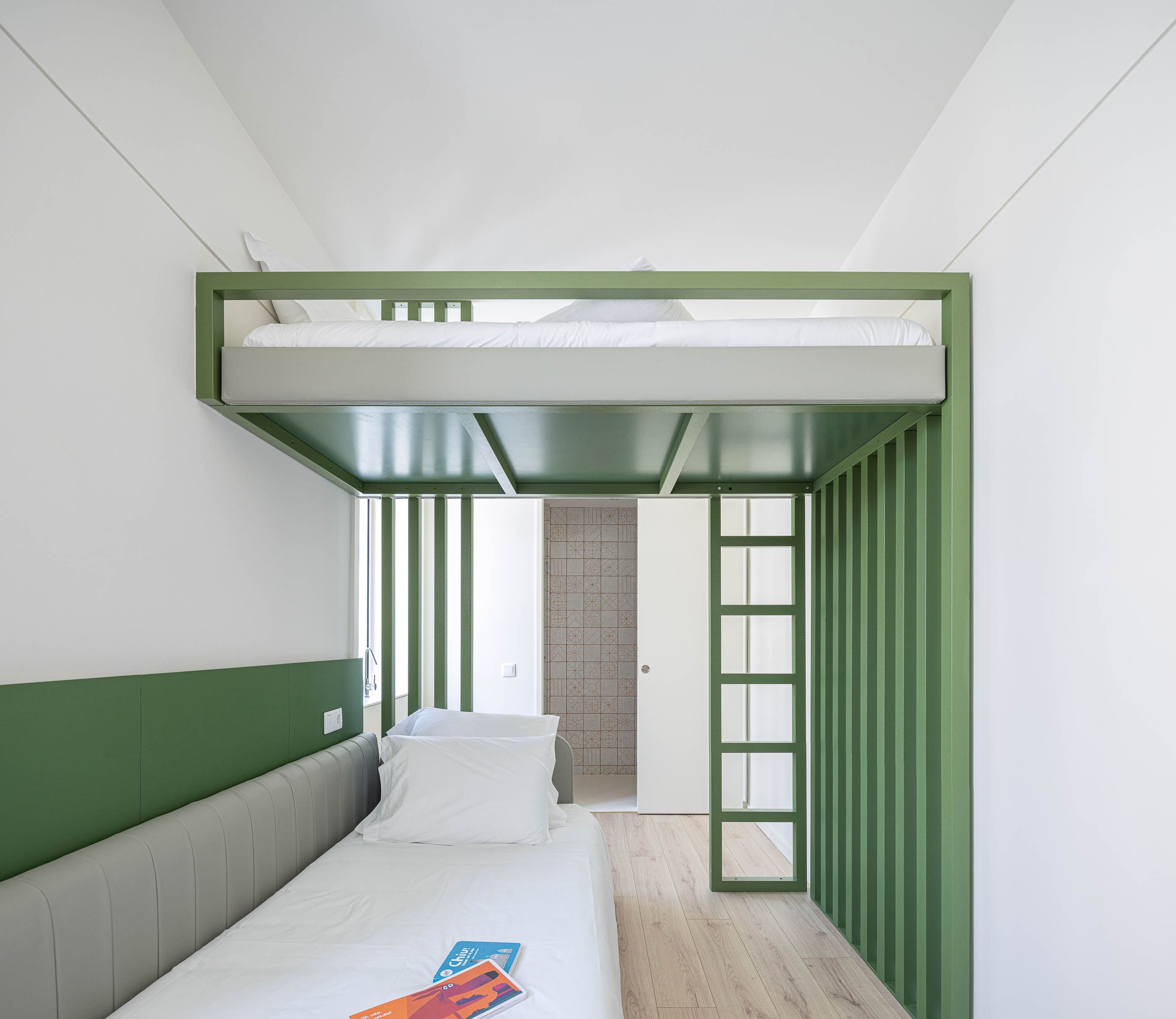 Quarto: Quarto com beliche verde, pavimento em madeira clara e casa de banho ao fundo. — A'mar arquitetura REM'A Arquitectos em Póvoa de Varzim