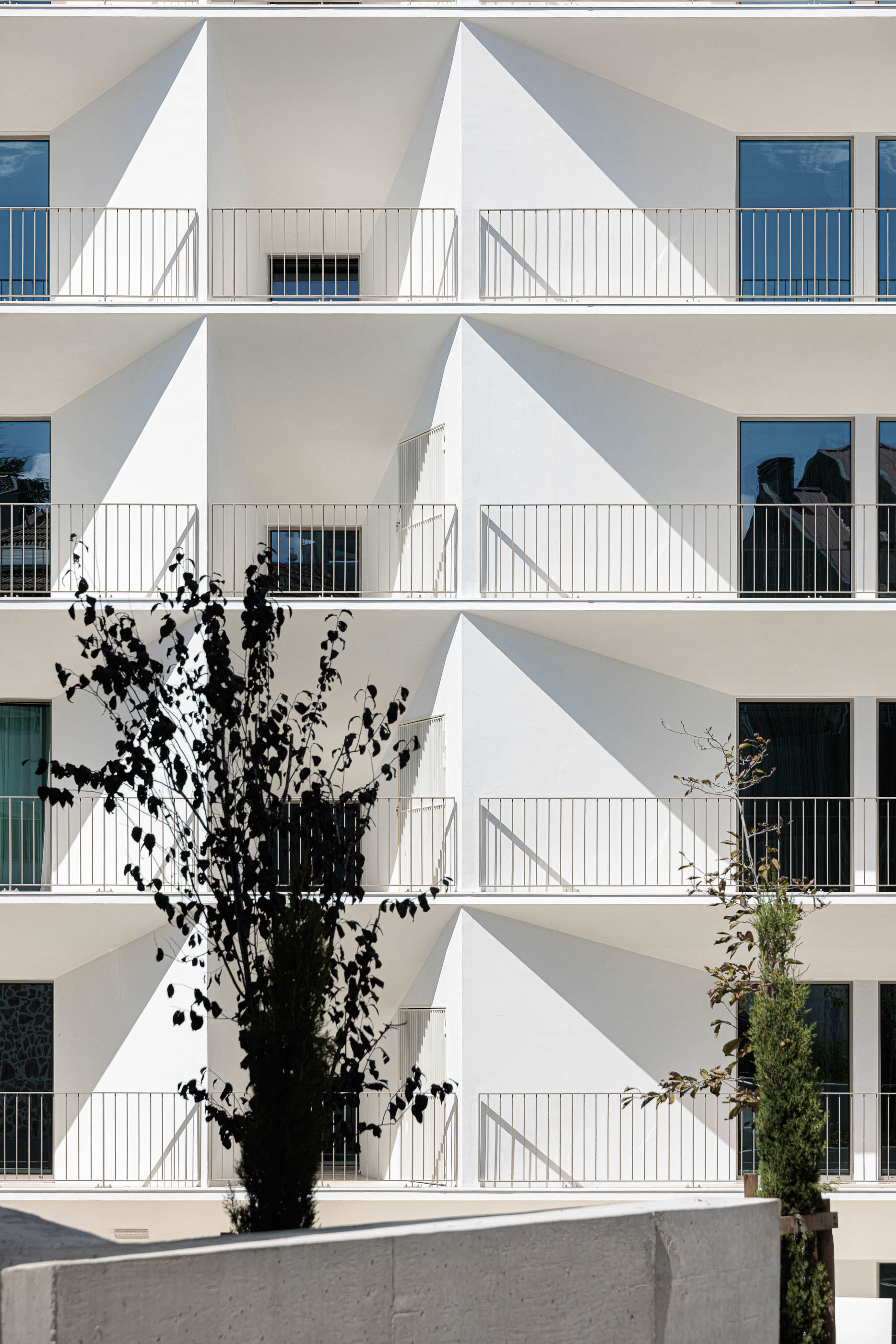 Fachada: Edifício branco com varandas triangulares, guardas metálicas e vegetação. — Varandas de Salgueiros arquitetura Floret Arquitectura em Porto