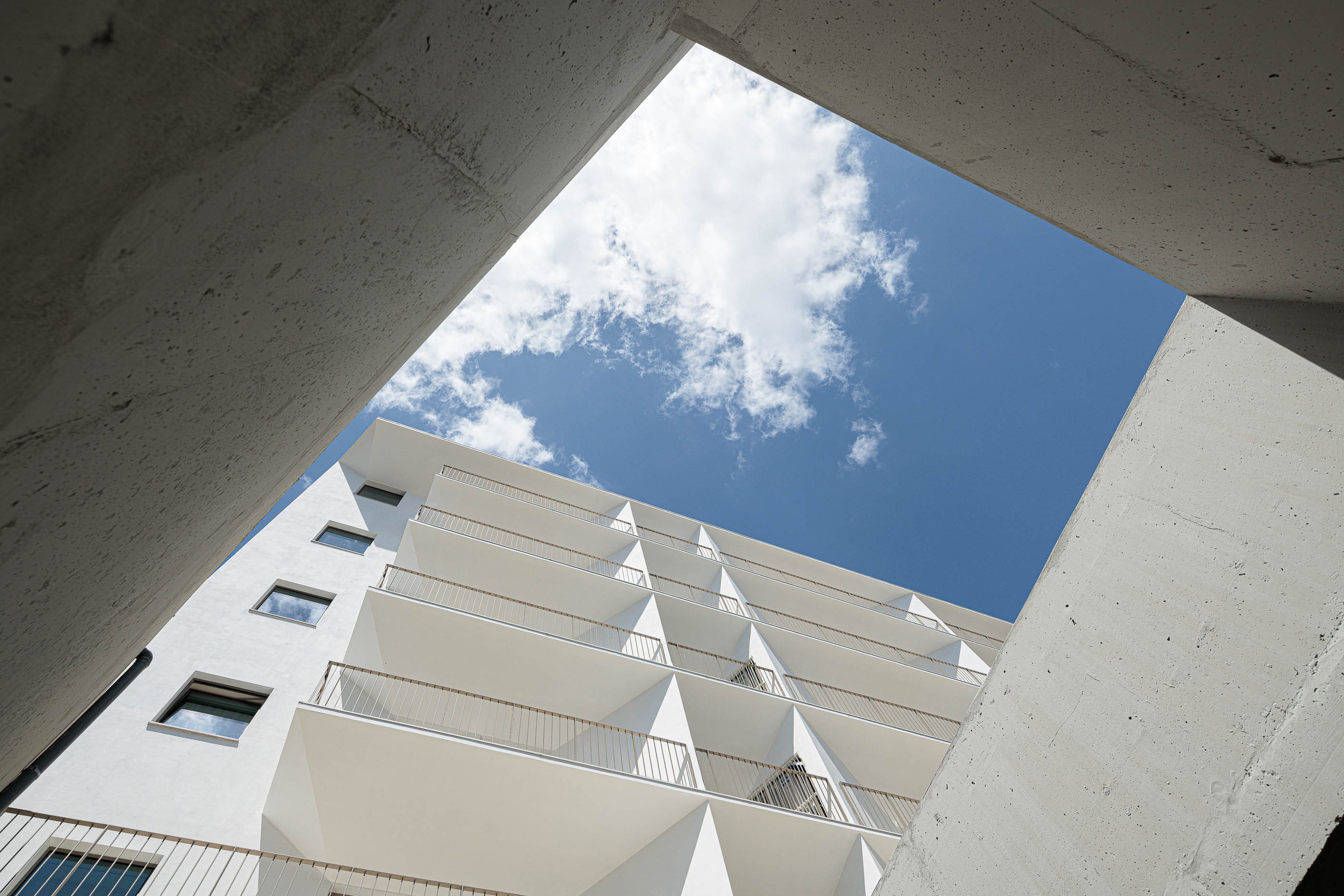 Exterior: Vista angular do edifício branco através de estrutura em betão. — Varandas de Salgueiros arquitetura Floret Arquitectura em Porto
