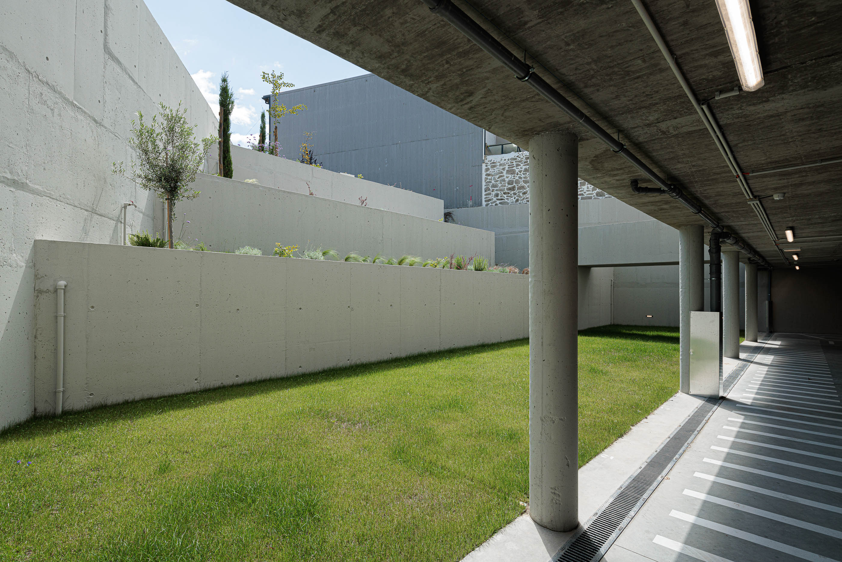 Garagem: Acesso à garagem com relvado, pilares de betão e iluminação. — Varandas de Salgueiros arquitetura Floret Arquitectura em Porto