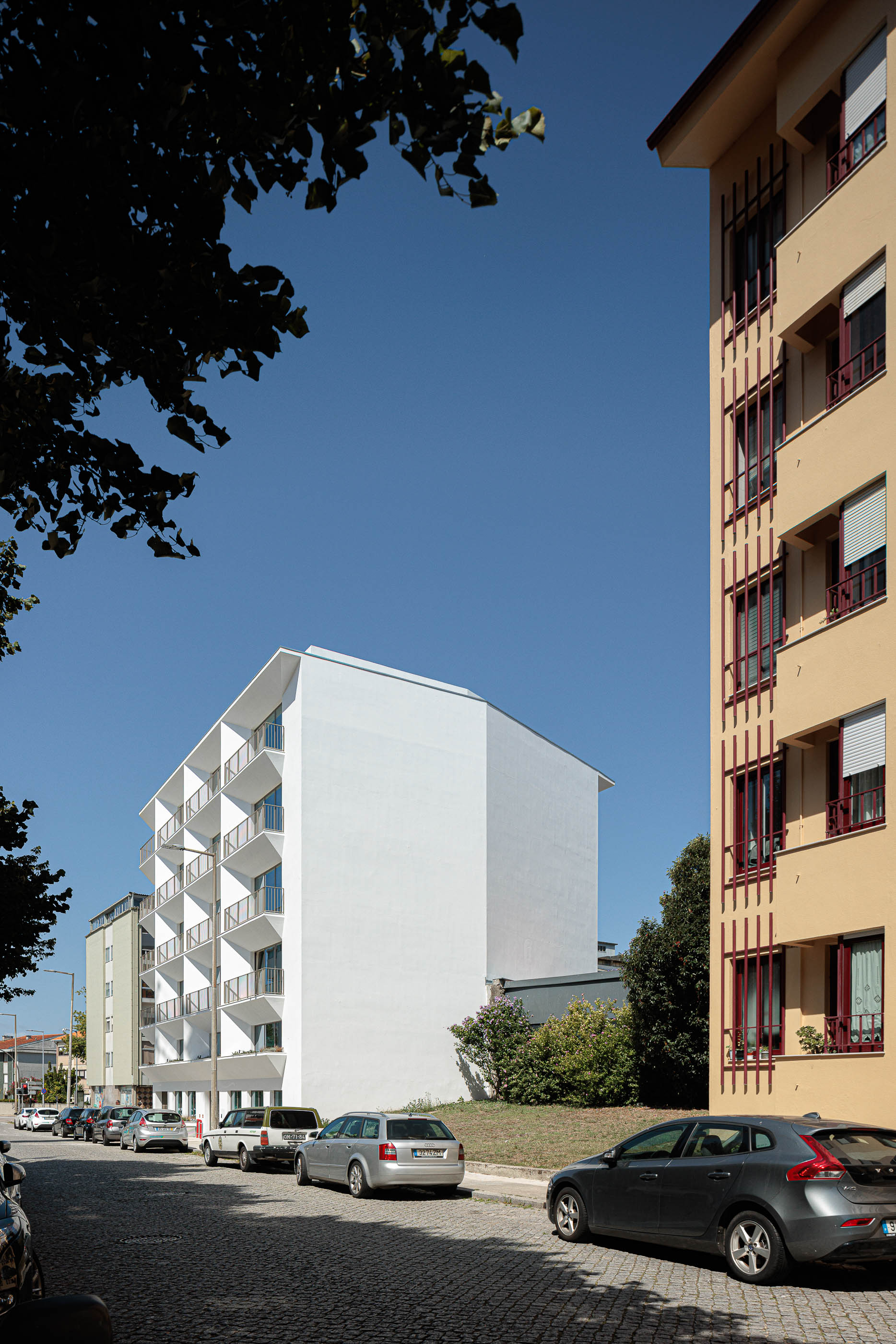 Exterior: Edifício branco com varandas triangulares visto da rua, com carros estacionados. — Varandas de Salgueiros arquitetura Floret Arquitectura em Porto