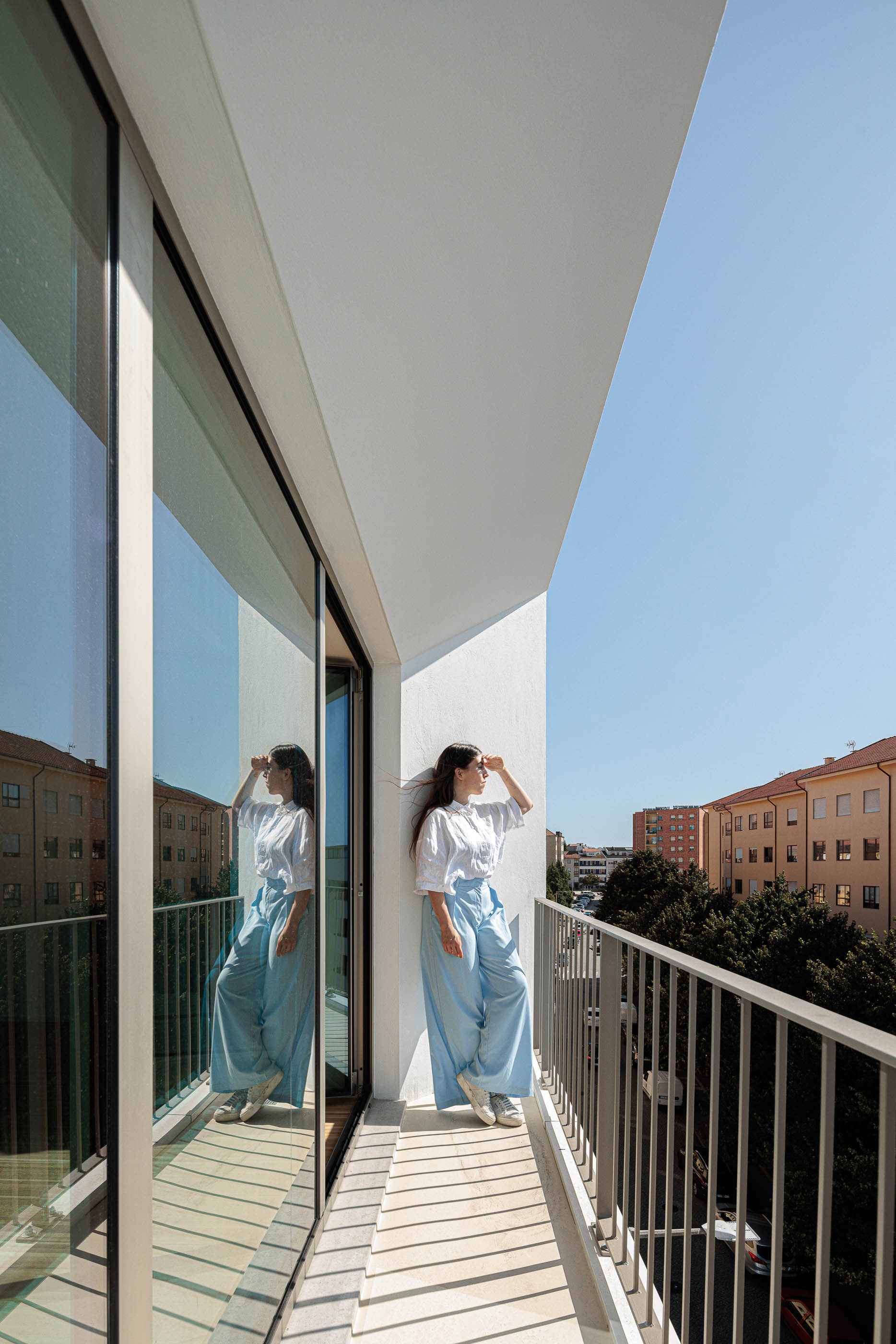Varanda: Mulher encostada à parede, com guarda metálica e vista para a cidade. — Varandas de Salgueiros arquitetura Floret Arquitectura em Porto