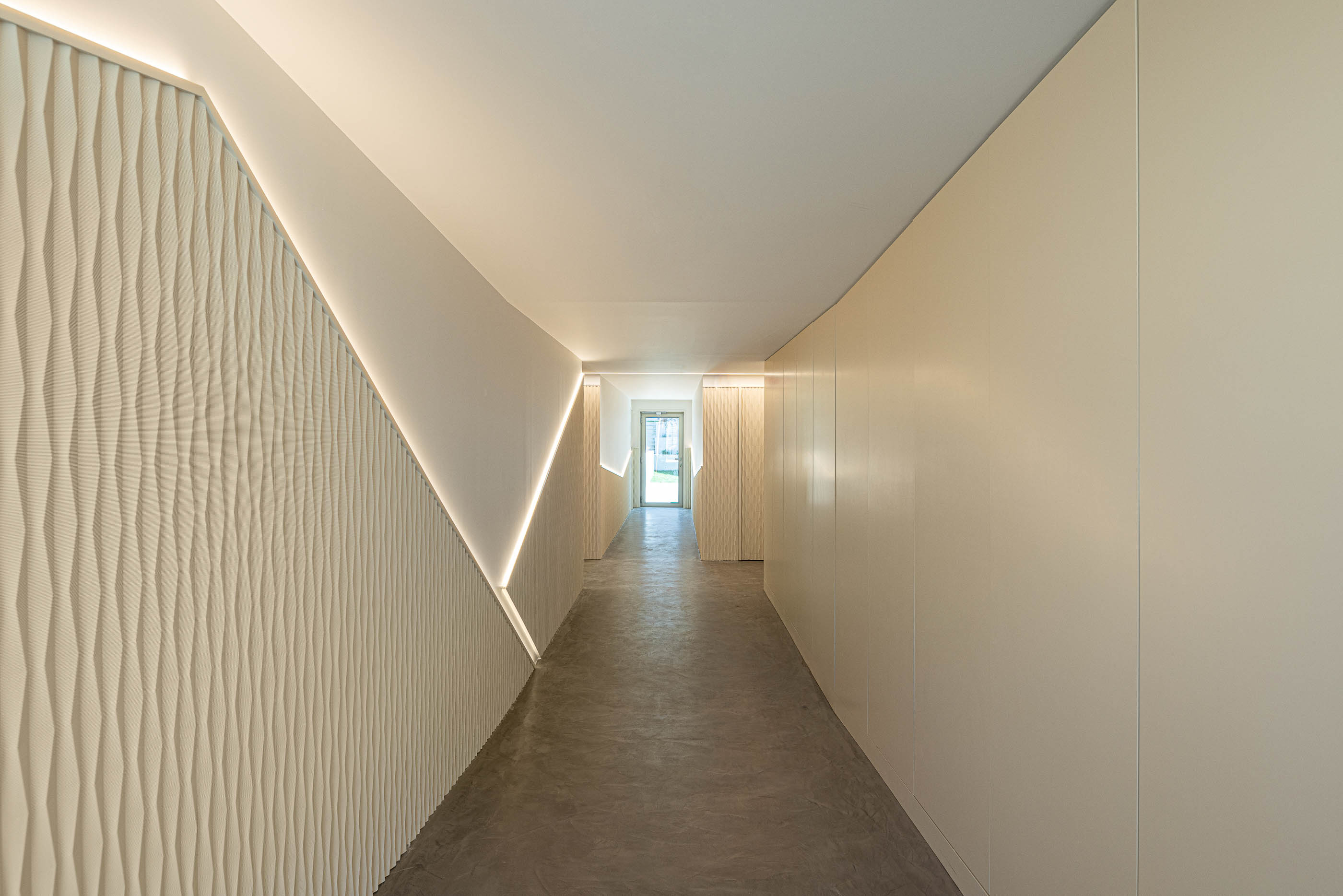 Corredor: Corredor com pavimento cinzento e paredes com revestimento texturado e luz indireta. — Varandas de Salgueiros arquitetura Floret Arquitectura em Porto