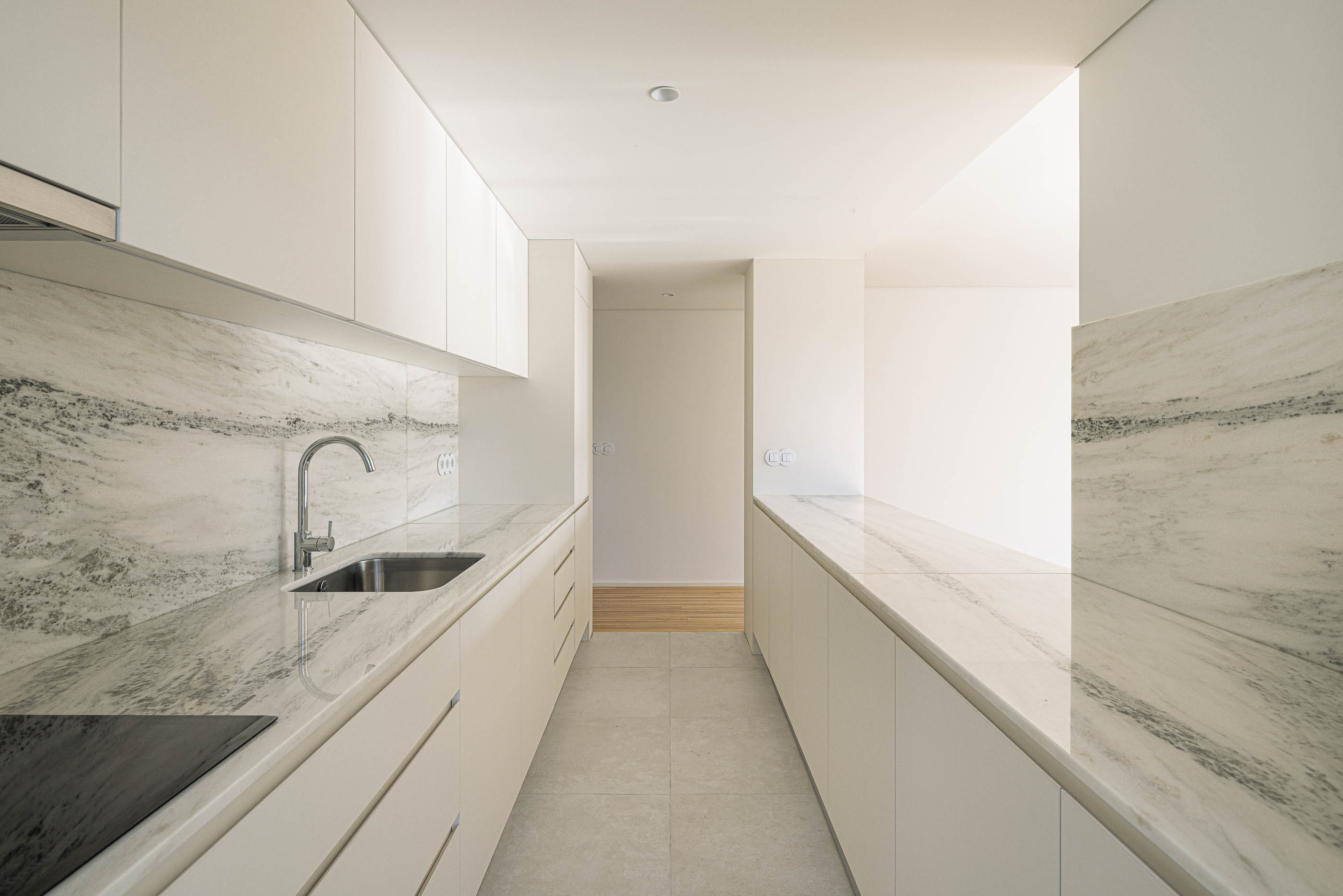 Cozinha: Cozinha comprida com bancada em mármore e armários brancos. — Varandas de Salgueiros arquitetura Floret Arquitectura em Porto