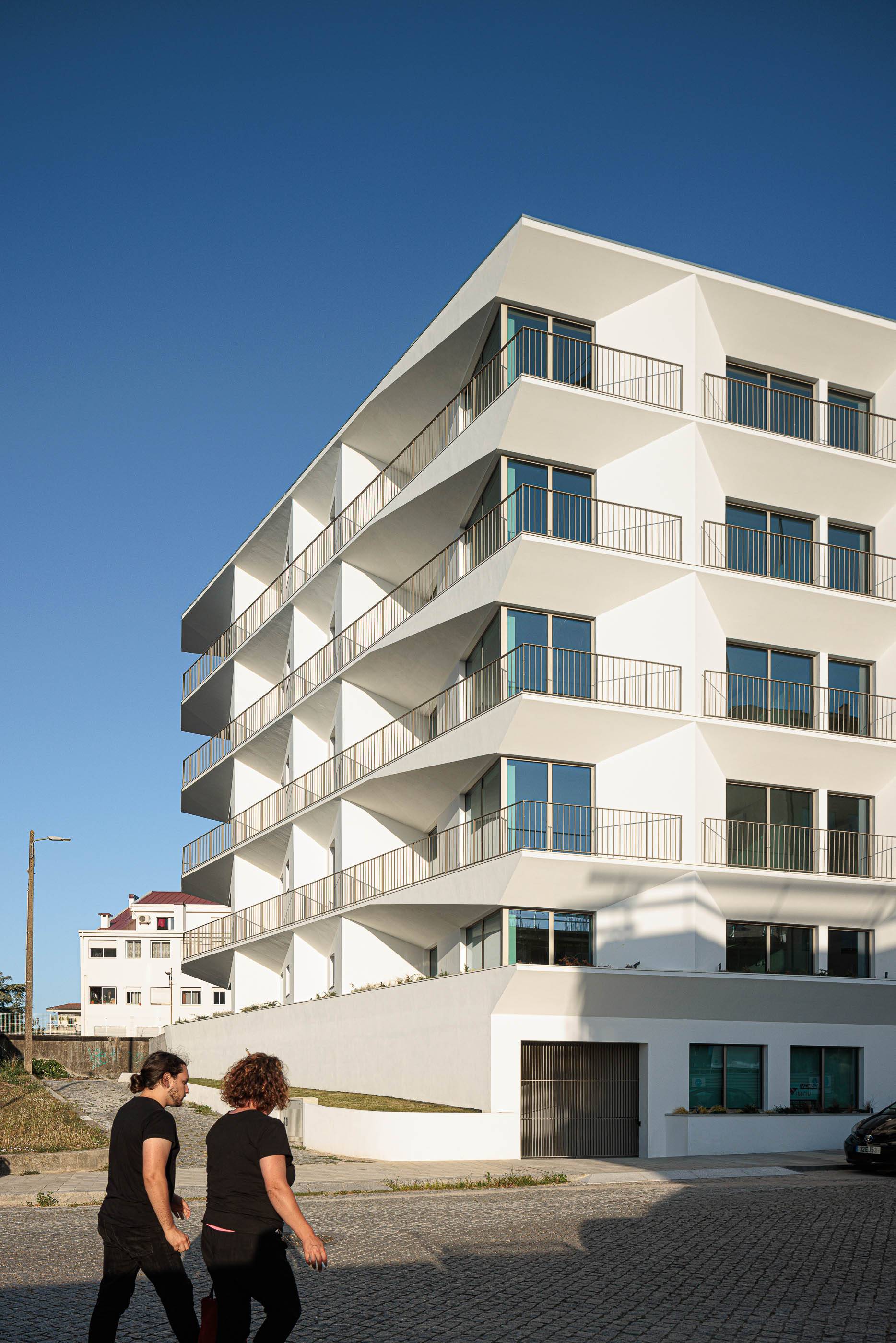 Exterior: Edifício branco com varandas triangulares e acesso à garagem. — Varandas de Salgueiros arquitetura Floret Arquitectura em Porto