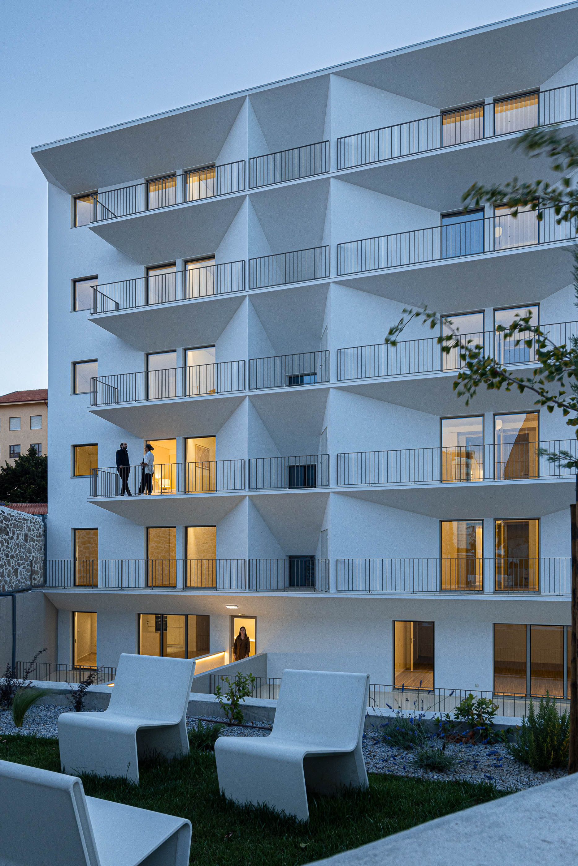 Exterior: Edifício branco com varandas triangulares, jardim e cadeiras brancas. — Varandas de Salgueiros arquitetura Floret Arquitectura em Porto