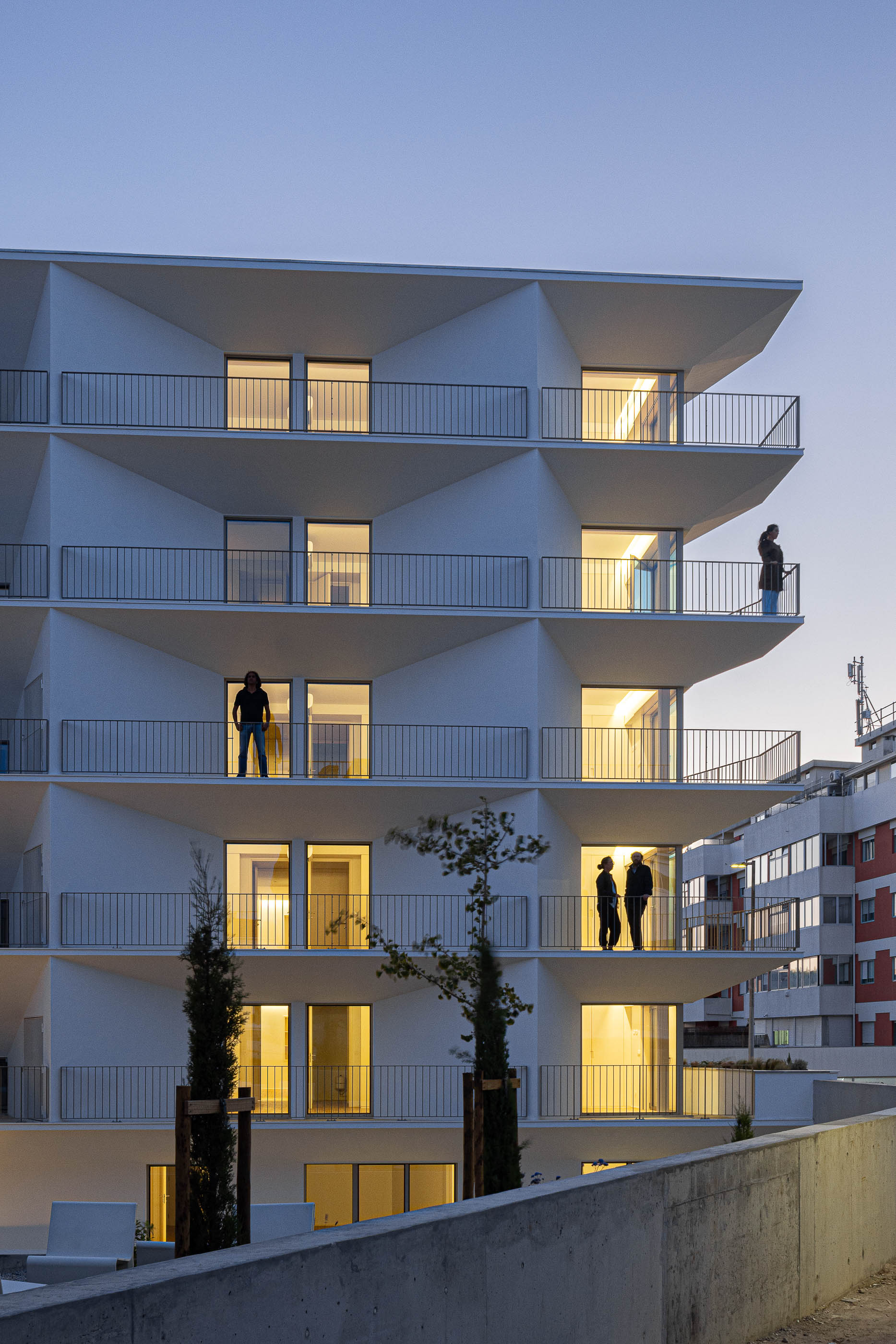 Exterior: Edifício branco com varandas triangulares iluminadas ao entardecer. — Varandas de Salgueiros arquitetura Floret Arquitectura em Porto