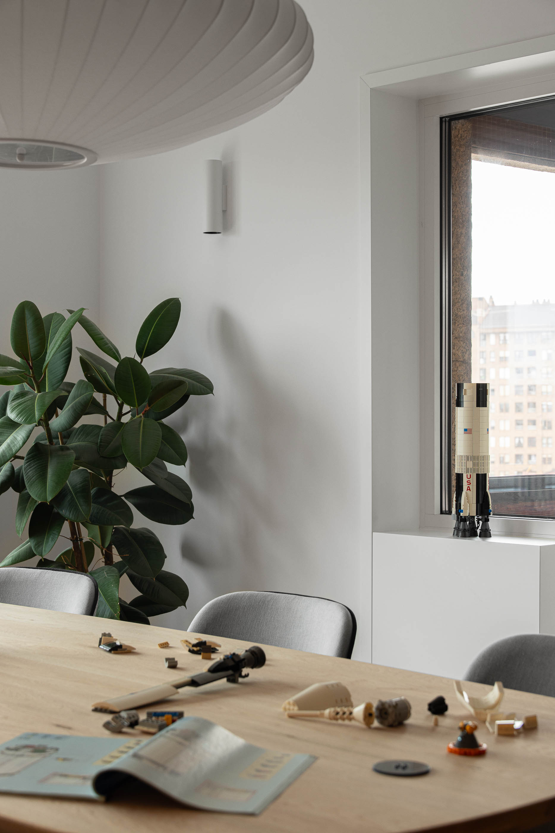 Sala de jantar, detalhe da mesa com objetos e planta. Candeeiro suspenso e janela com vista urbana. — Reforma apartamento CP em Avilés arquitetura David Olmos Arquitectos em Avilés
