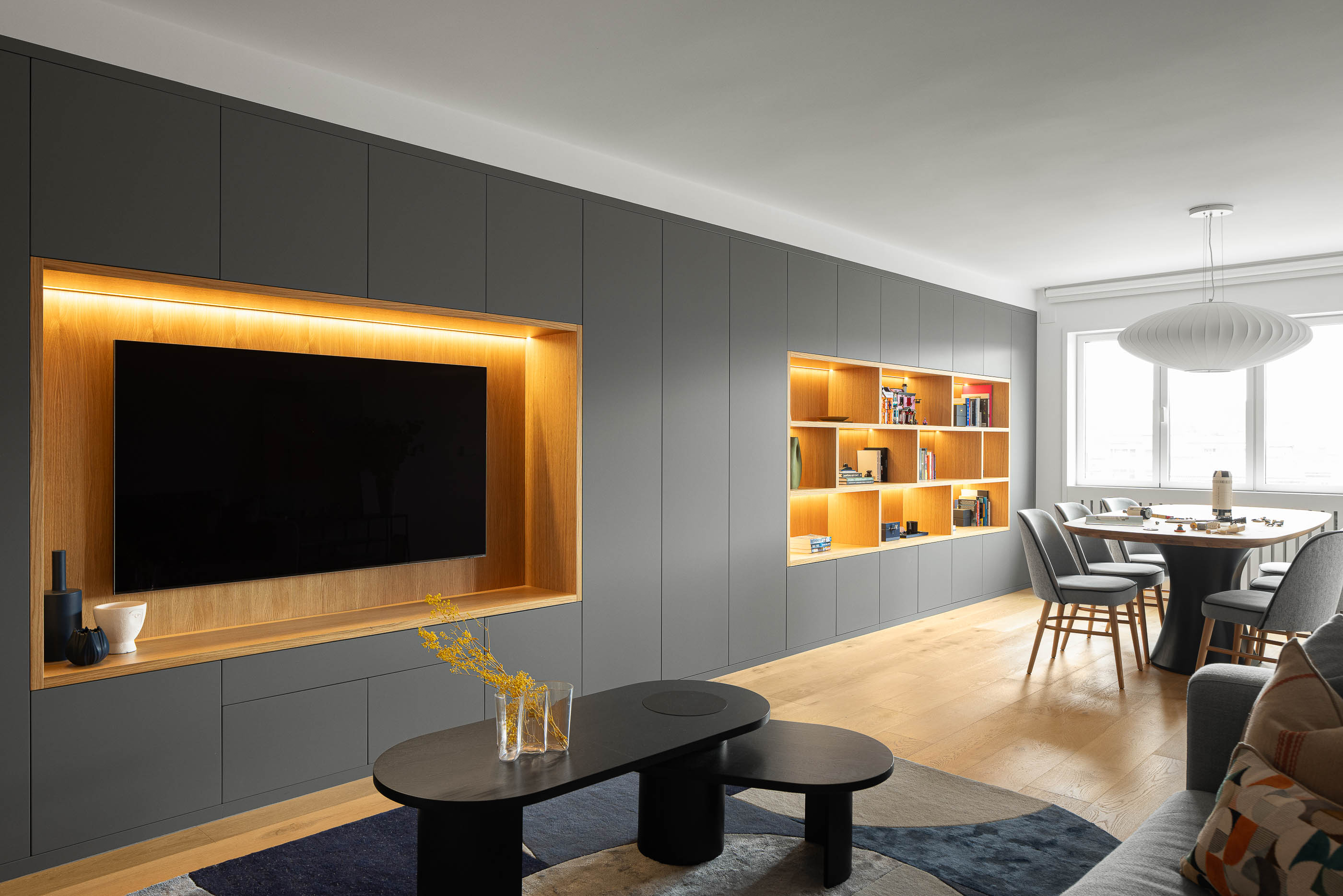 Sala de estar com móvel cinzento embutido, televisão e estante iluminada. Mesa de centro preta e alcatifa geométrica. — Reforma apartamento CP em Avilés arquitetura David Olmos Arquitectos em Avilés