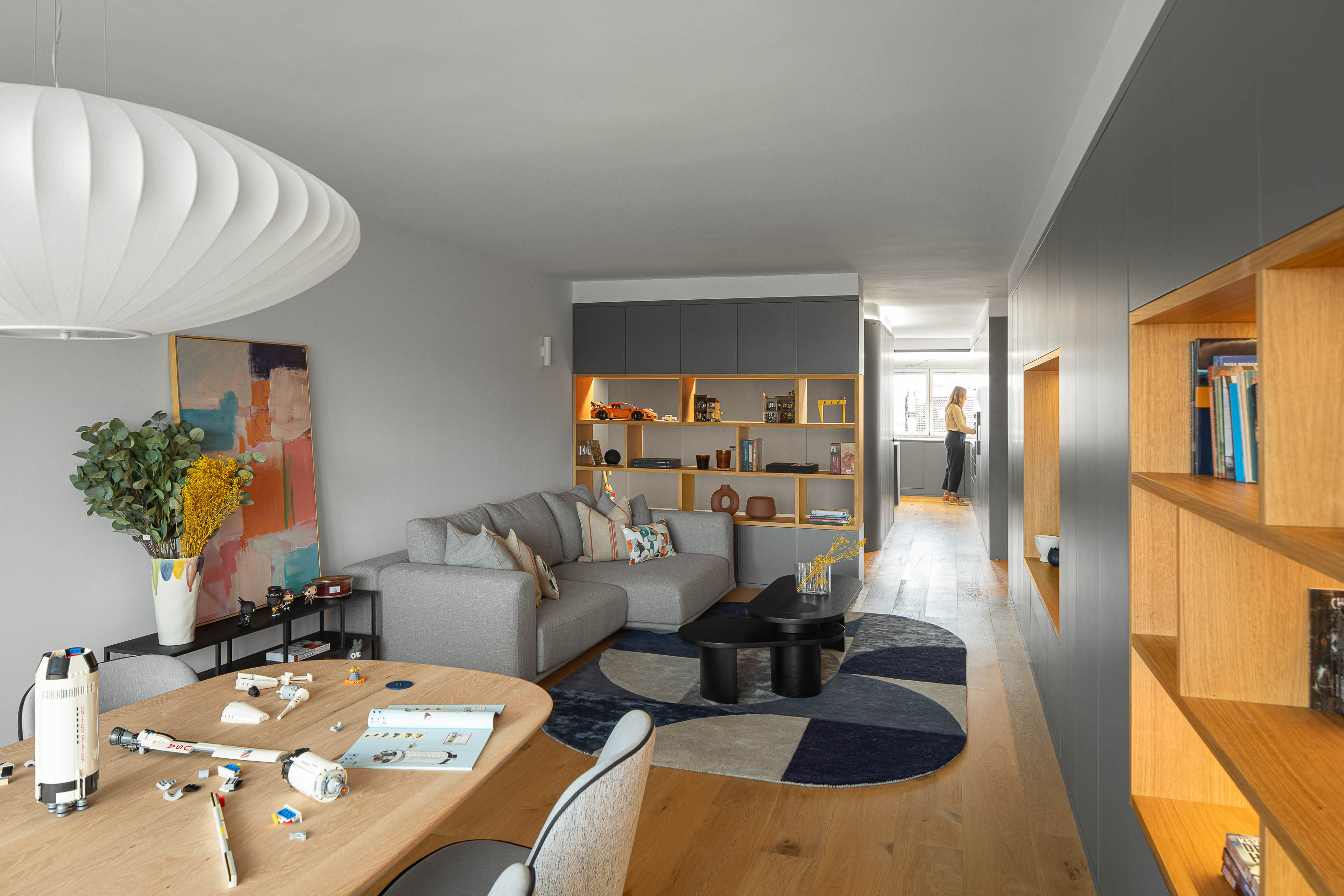 Sala de estar e jantar com sofá cinzento, mesa de centro, alcatifa geométrica e estante embutida. Pavimento em madeira clara. — Reforma apartamento CP em Avilés arquitetura David Olmos Arquitectos em Avilés