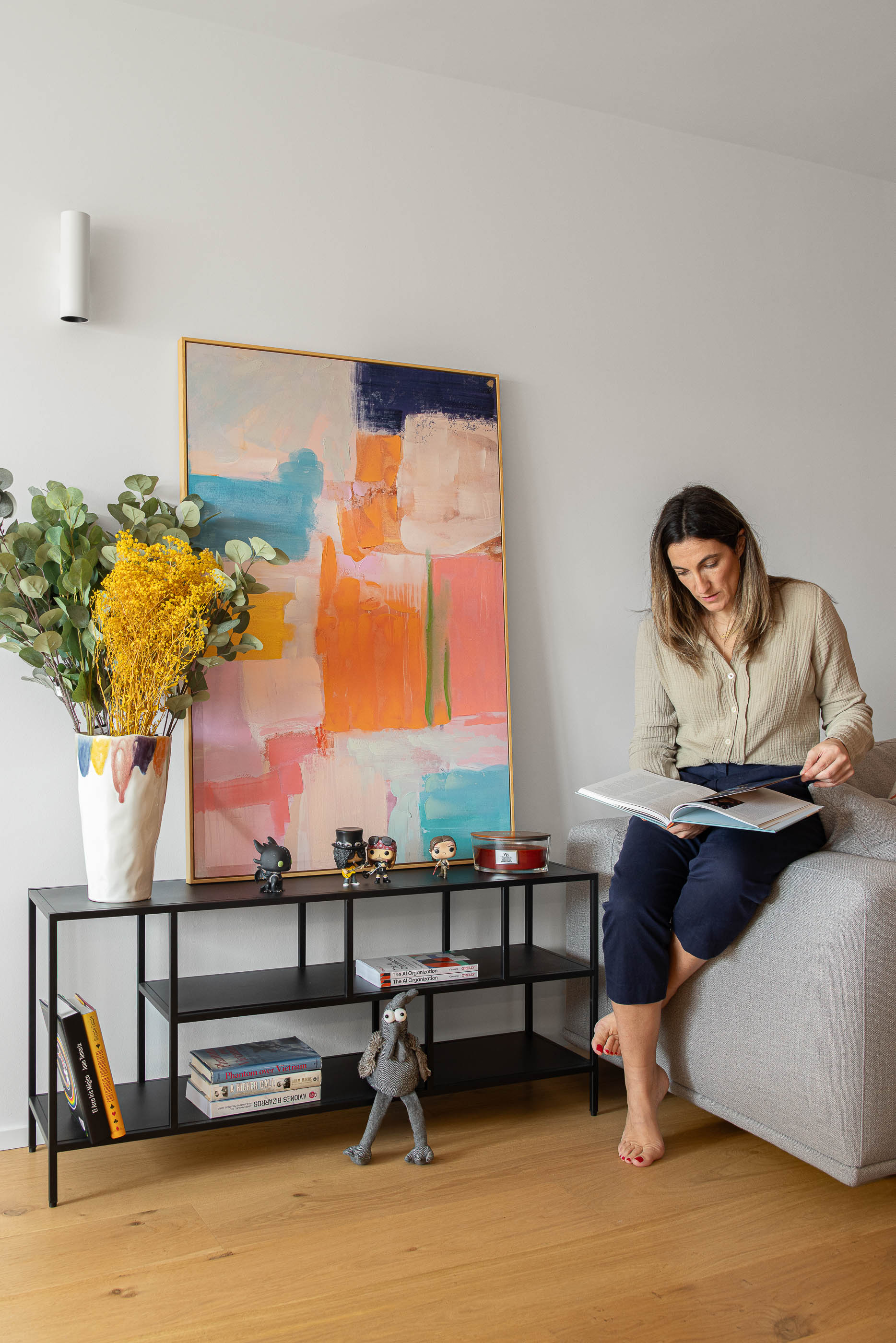 Sala de estar com estante preta, pintura colorida e vaso com flores amarelas. Pavimento em madeira clara. — Reforma apartamento CP em Avilés arquitetura David Olmos Arquitectos em Avilés