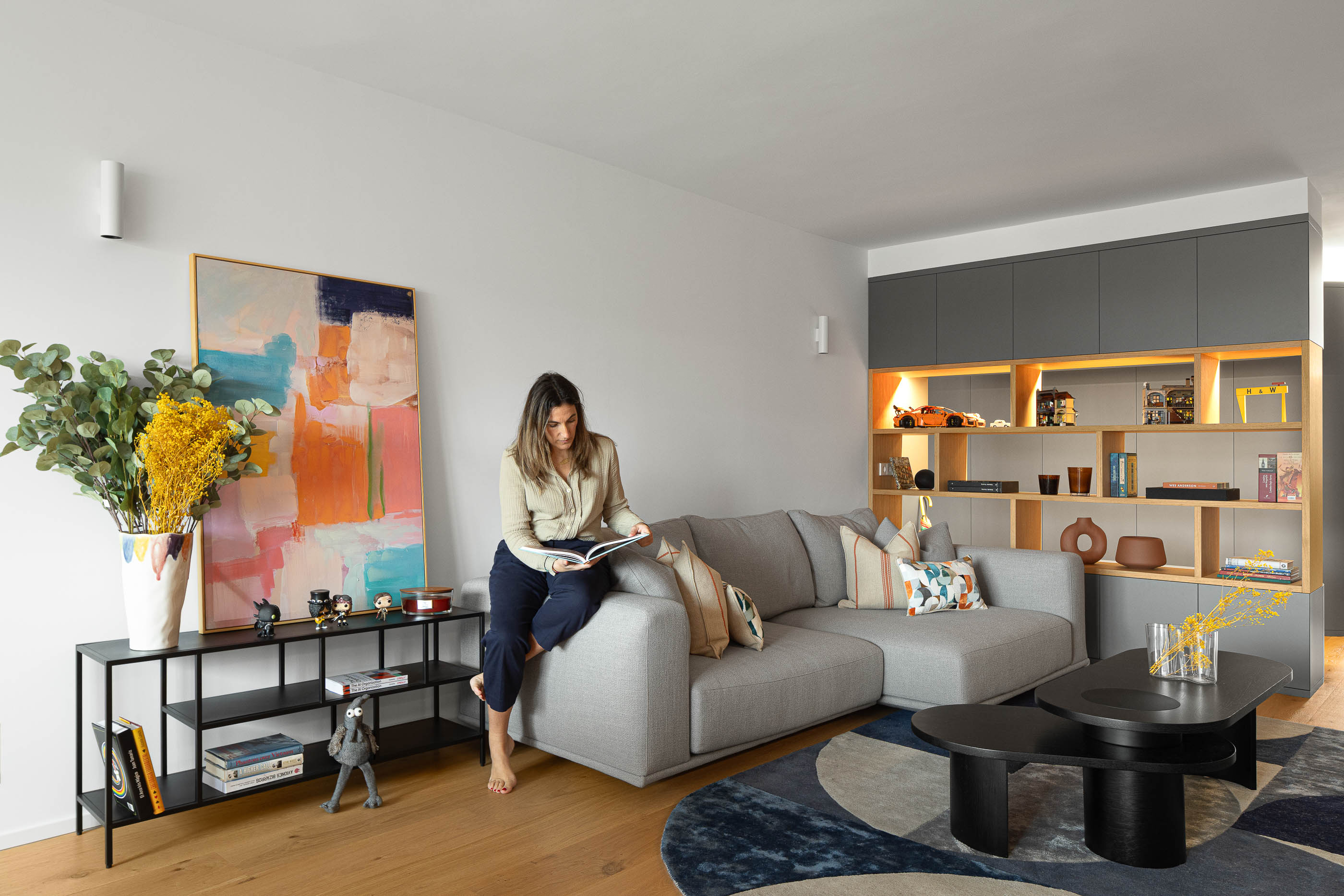 Sala de estar com sofá cinzento, mesa de centro preta, alcatifa geométrica e estante embutida. Pavimento em madeira clara. — Reforma apartamento CP em Avilés arquitetura David Olmos Arquitectos em Avilés