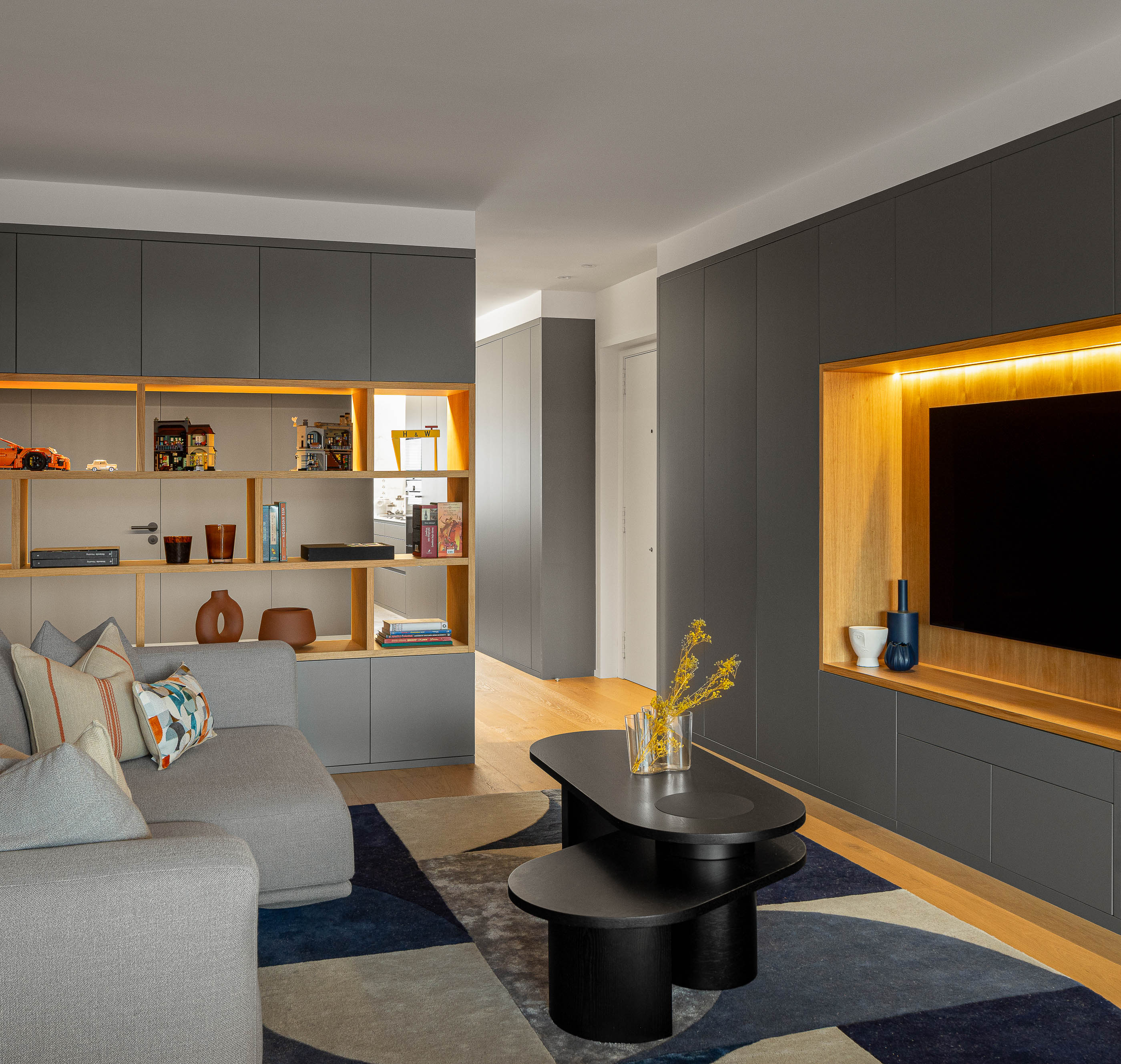 Sala de estar com sofá cinzento, mesa de centro preta, alcatifa geométrica e móvel cinzento embutido. — Reforma apartamento CP em Avilés arquitetura David Olmos Arquitectos em Avilés
