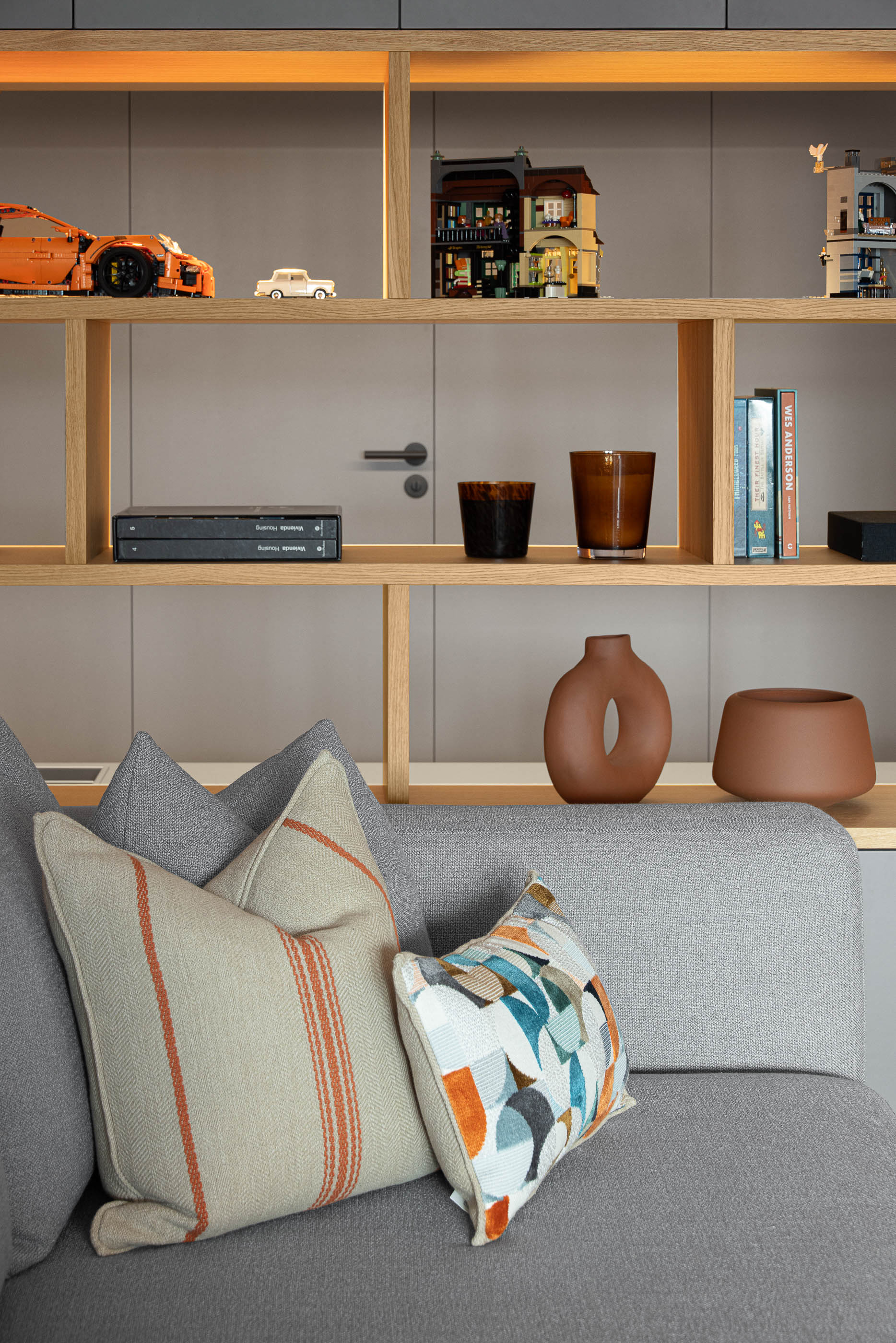 Sala de estar, detalhe de estante iluminada com objetos decorativos e almofadas no sofá cinzento. — Reforma apartamento CP em Avilés arquitetura David Olmos Arquitectos em Avilés