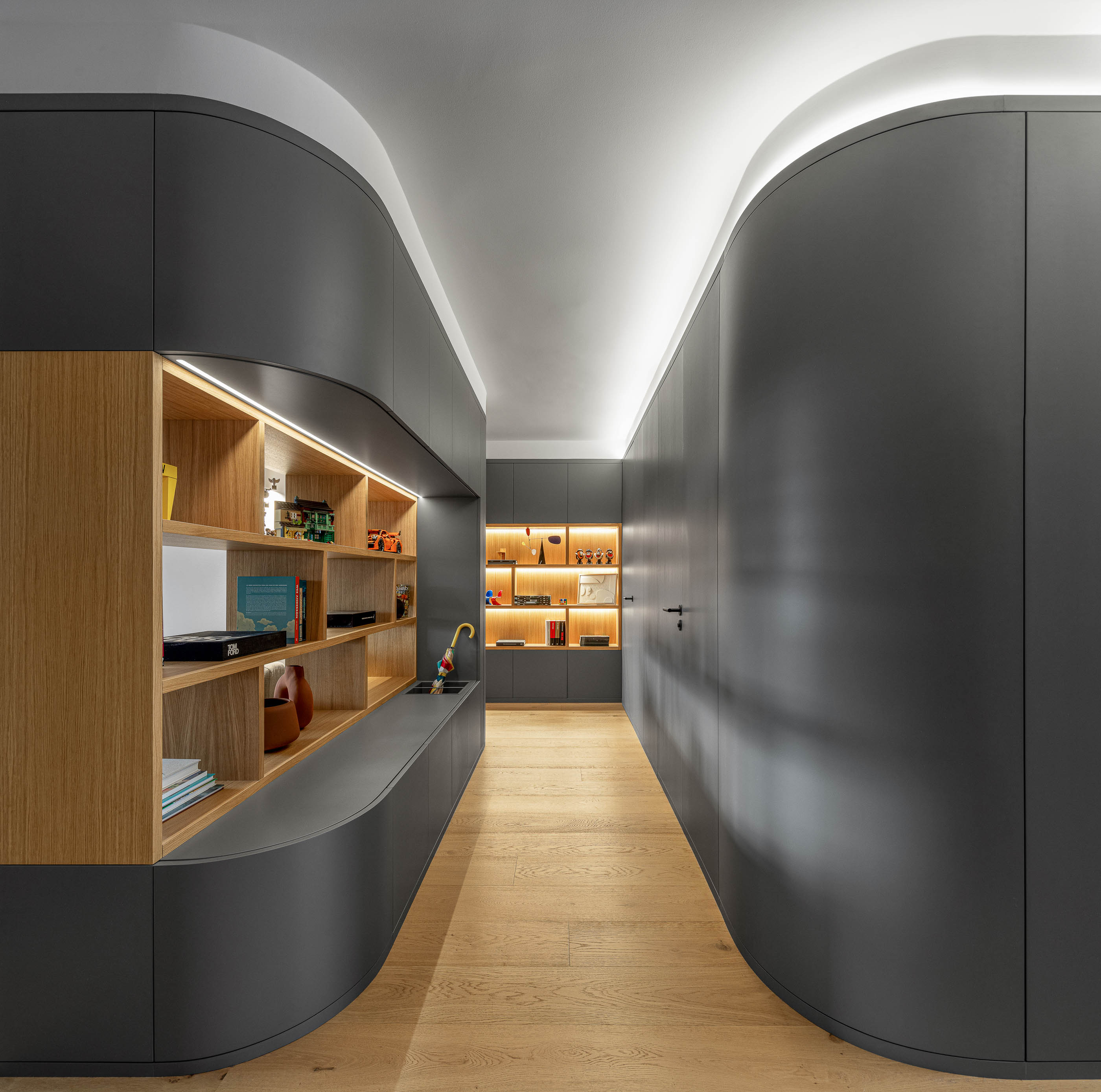 Corredor com móvel cinzento curvo, estantes iluminadas e pavimento em madeira clara. — Reforma apartamento CP em Avilés arquitetura David Olmos Arquitectos em Avilés