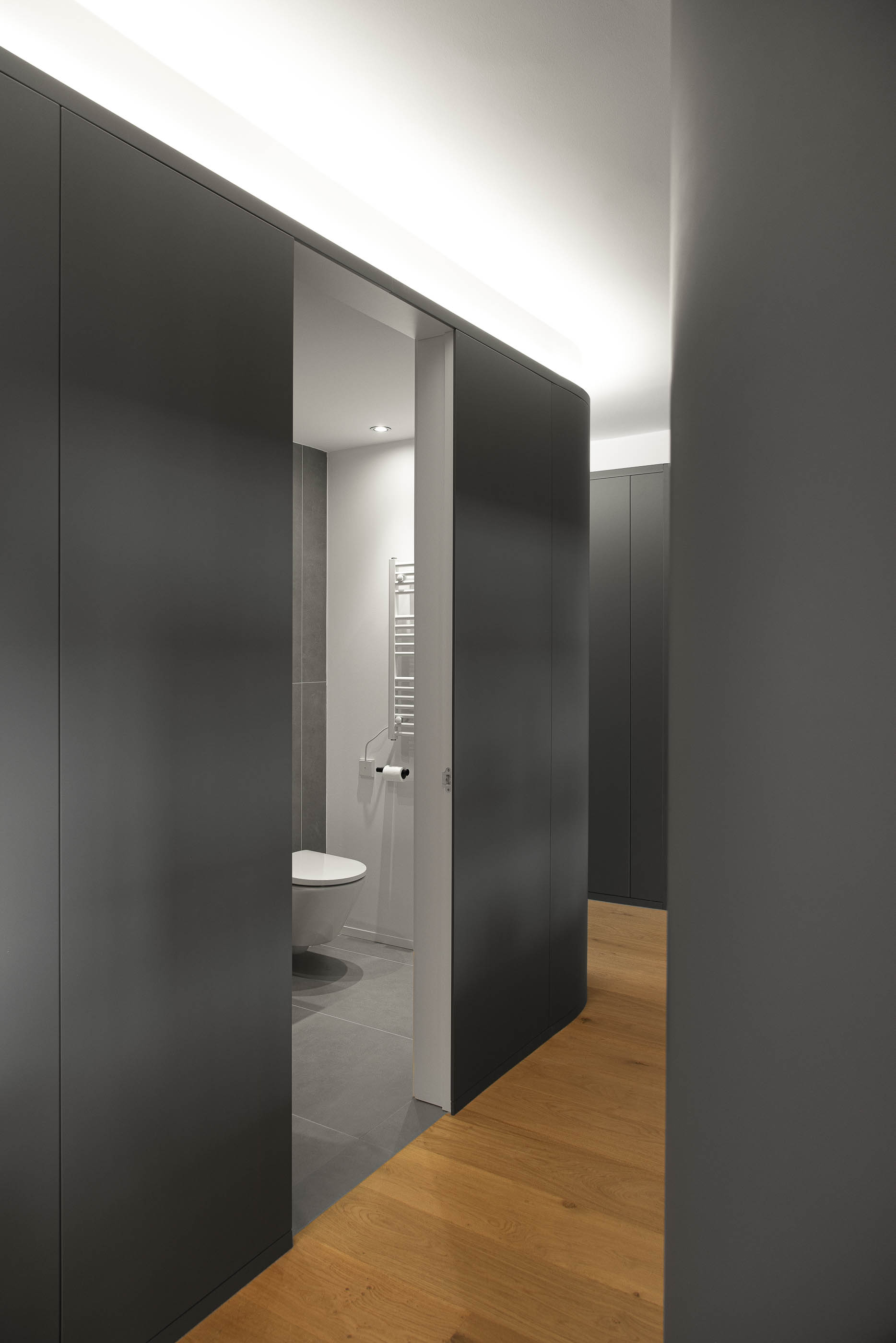 Corredor, vista para casa de banho com sanita e toalheiro aquecido. Pavimento em madeira clara e cerâmica cinzenta. — Reforma apartamento CP em Avilés arquitetura David Olmos Arquitectos em Avilés