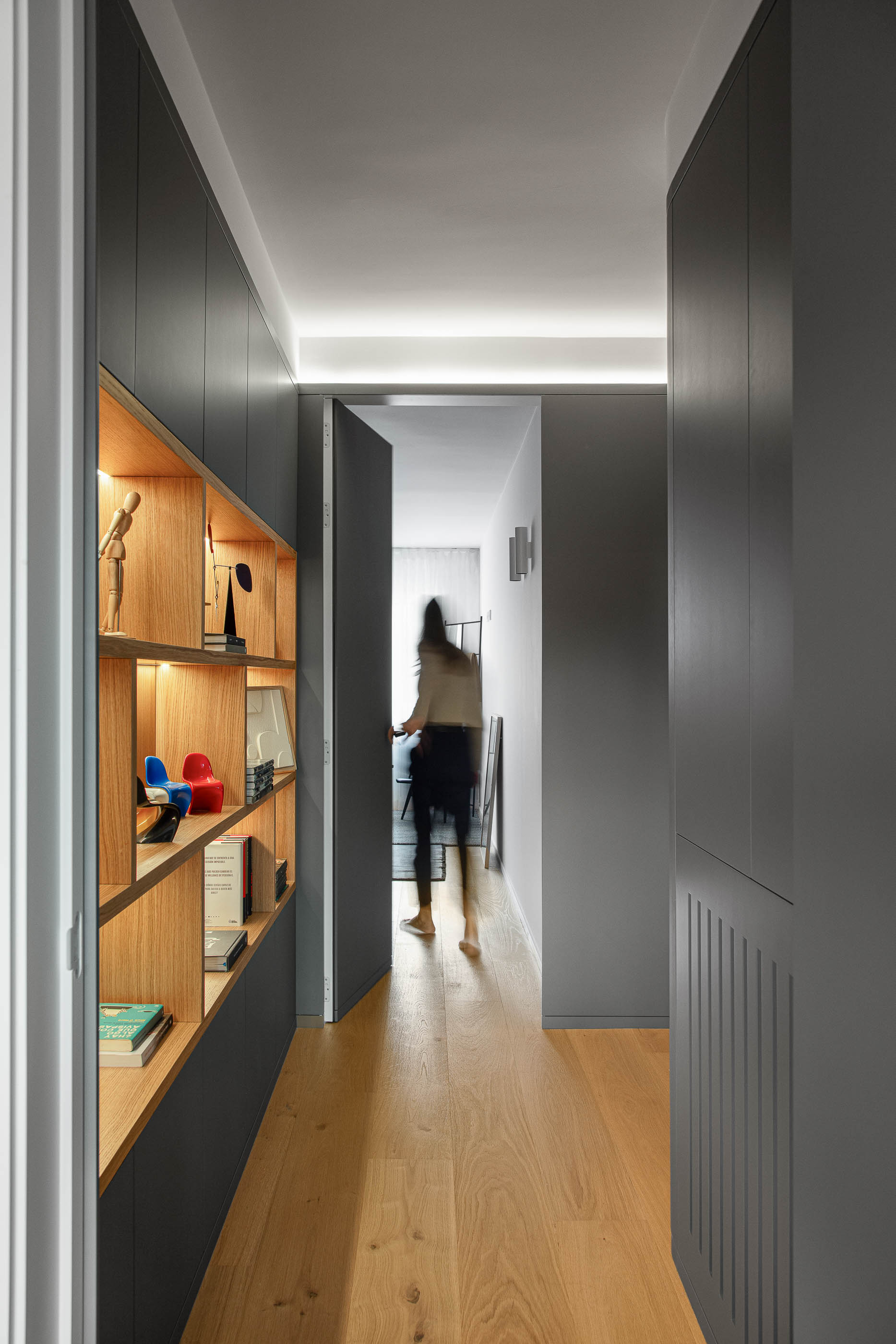 Corredor com estantes iluminadas e porta para divisão. Pavimento em madeira clara. — Reforma apartamento CP em Avilés arquitetura David Olmos Arquitectos em Avilés