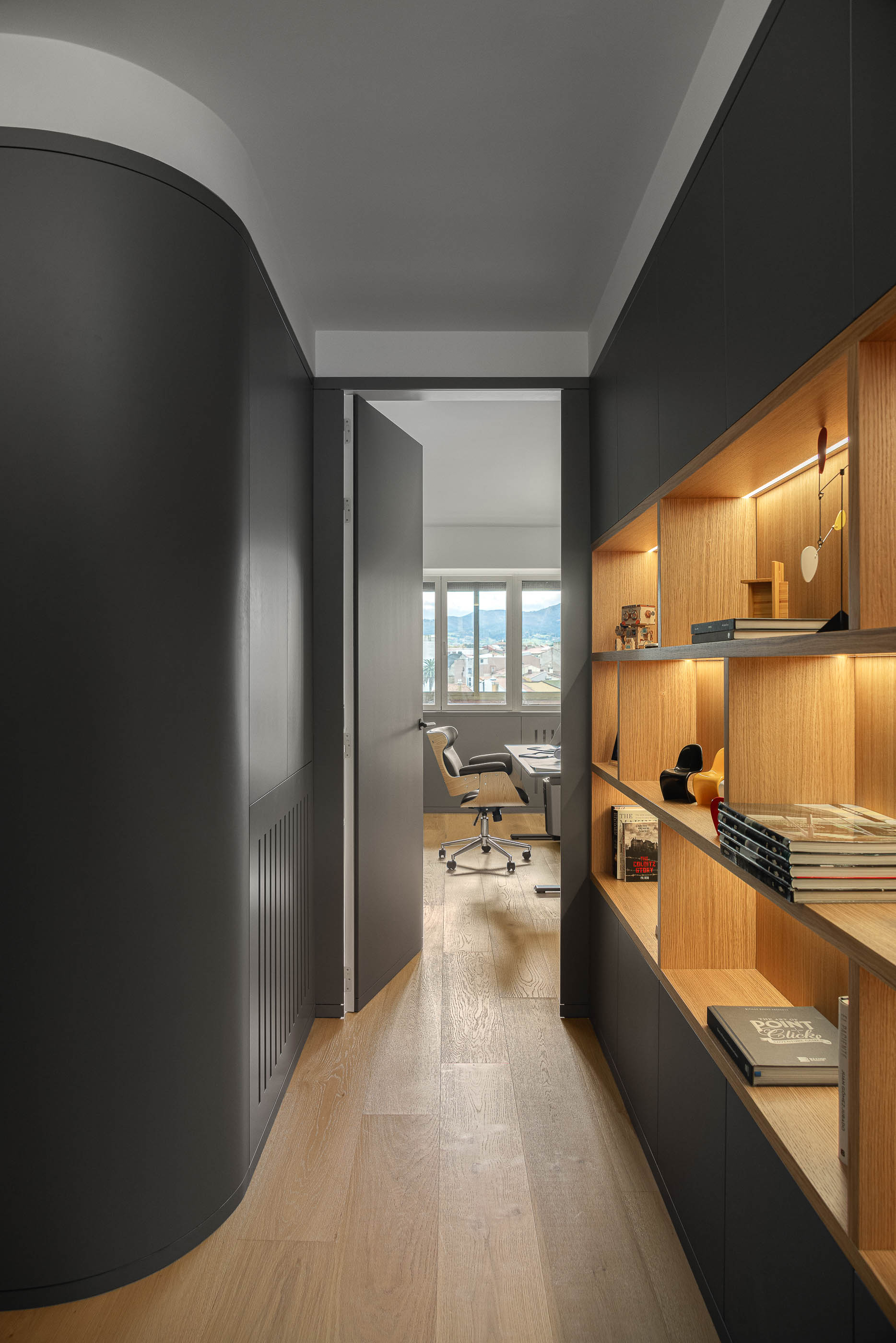 Corredor com estantes iluminadas e porta para escritório. Pavimento em madeira clara. — Reforma apartamento CP em Avilés arquitetura David Olmos Arquitectos em Avilés