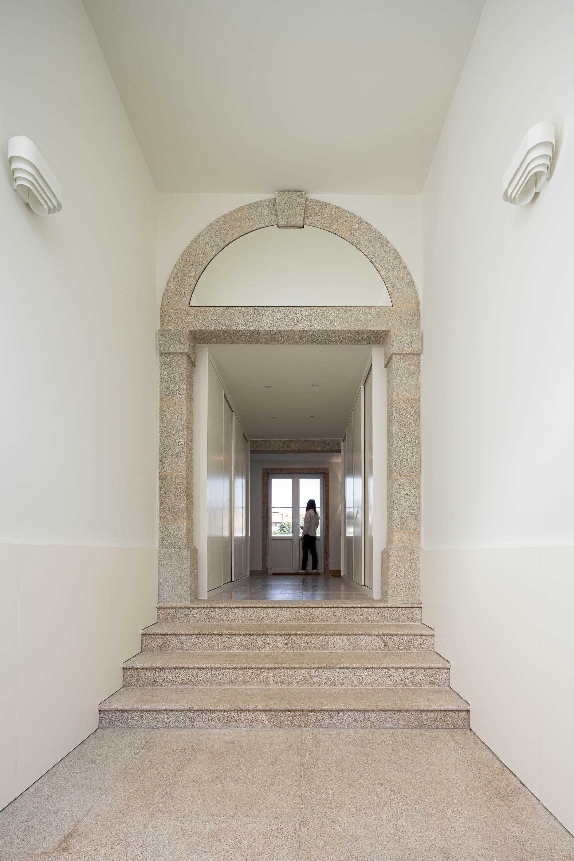 Hall de entrada: Arco em pedra rústica, pavimento em mosaico e candeeiros de parede modernos. — Condomínio das Artes arquitetura MiMool Arquitectura & Interiores em Porto