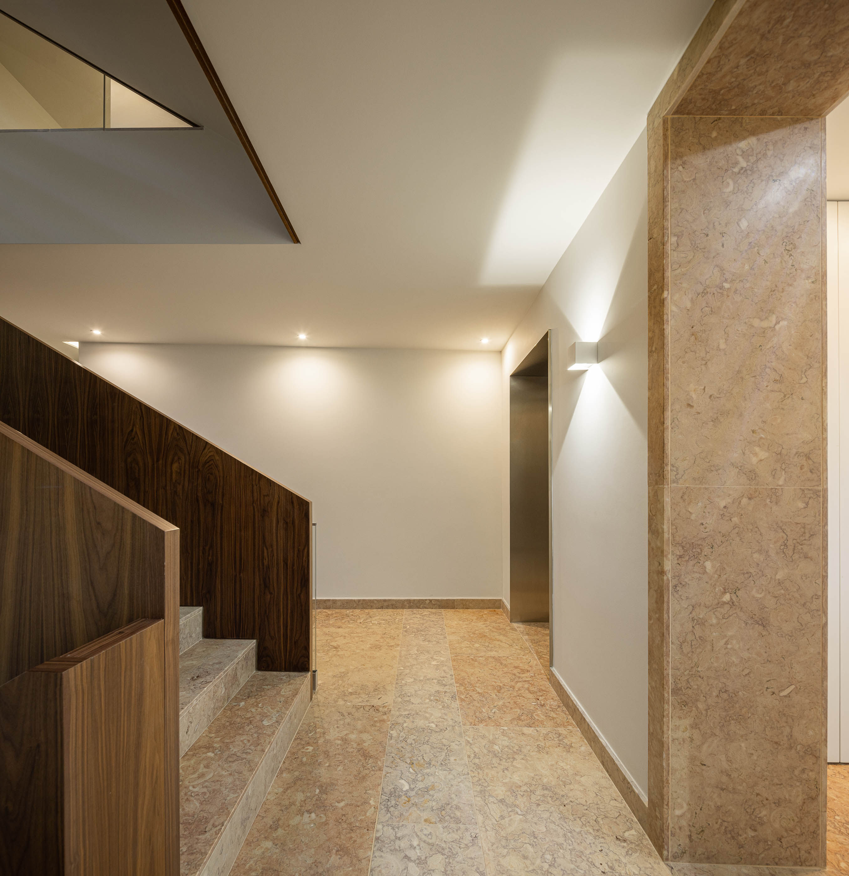 Escadas: Corrimão em madeira escura, pavimento em mármore e iluminação embutida. — Condomínio das Artes arquitetura MiMool Arquitectura & Interiores em Porto