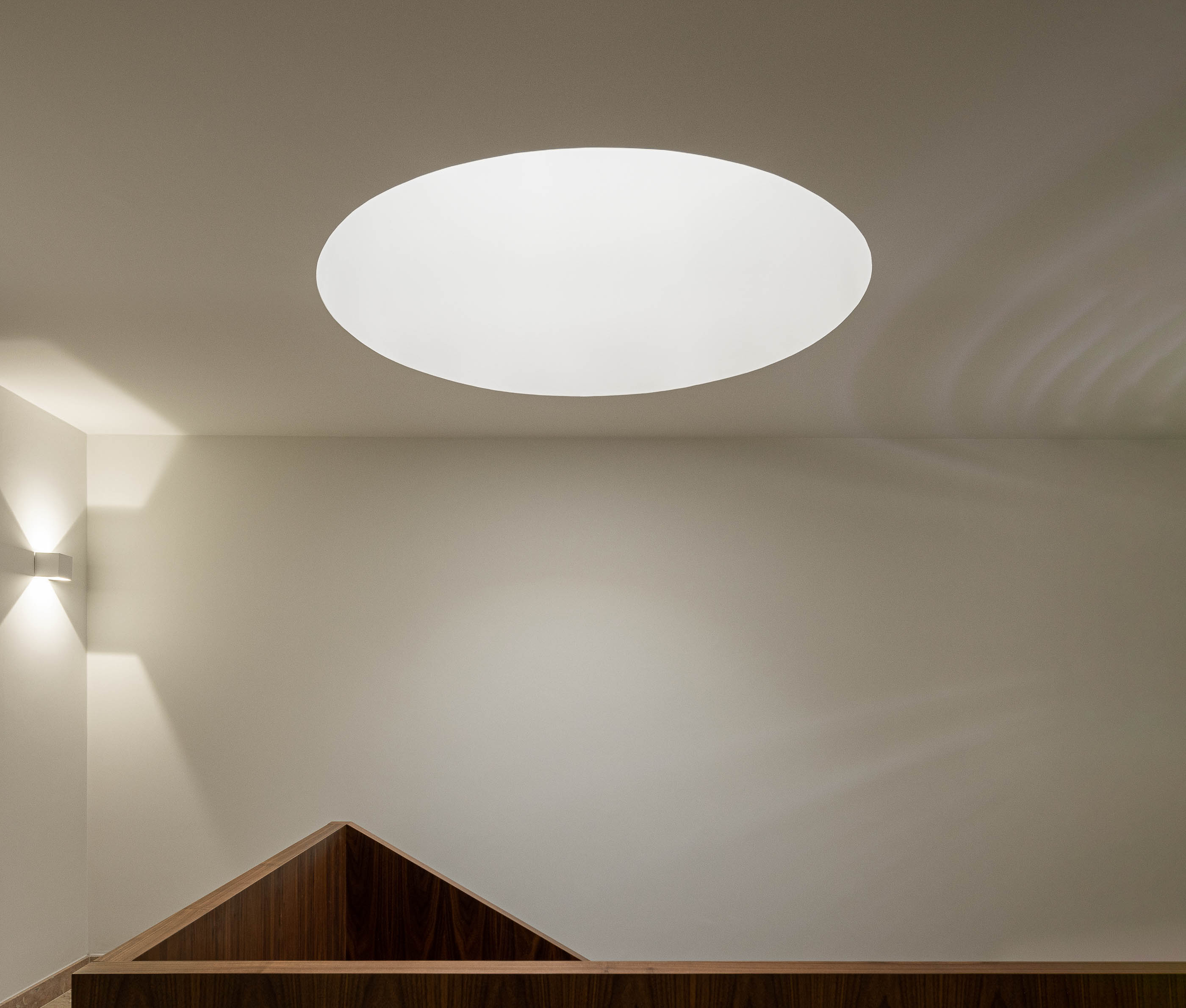 Escadas: Candeeiro circular embutido no teto, paredes brancas e corrimão em madeira escura. — Condomínio das Artes arquitetura MiMool Arquitectura & Interiores em Porto