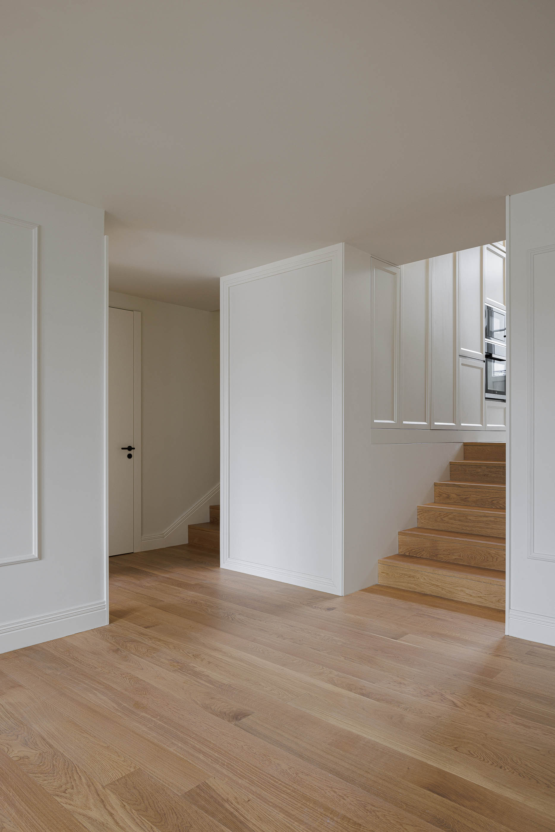Sala de estar: Pavimento em madeira clara, paredes brancas com molduras e escadas ao fundo. — Condomínio das Artes arquitetura MiMool Arquitectura & Interiores em Porto