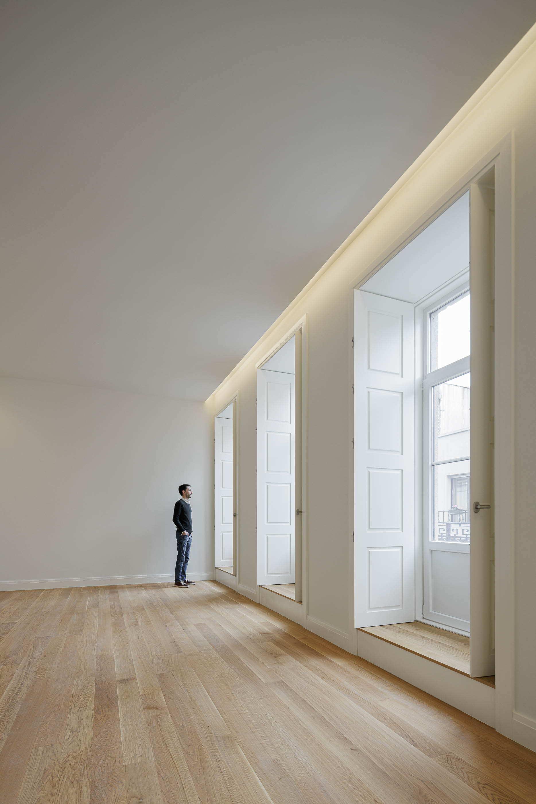 Sala de estar: Três janelas altas com portadas brancas e pavimento em madeira clara. — Condomínio das Artes arquitetura MiMool Arquitectura & Interiores em Porto