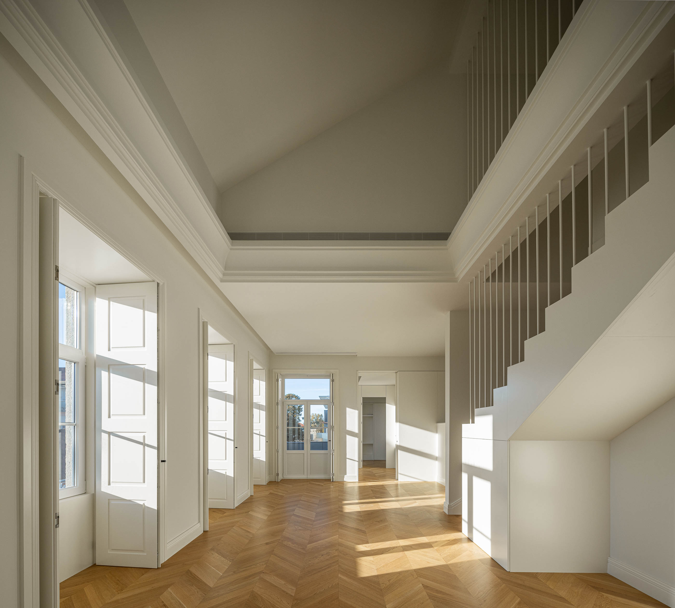 Sala de estar: Escadas com corrimão branco, pavimento em madeira espinha de peixe e janelas com portadas. — Condomínio das Artes arquitetura MiMool Arquitectura & Interiores em Porto