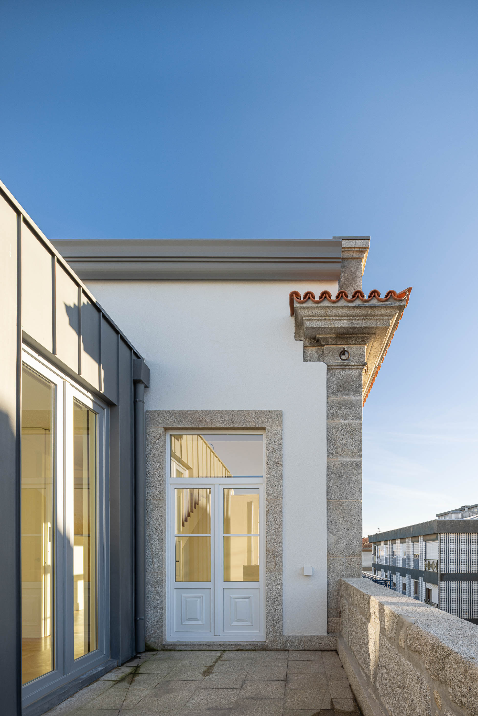 Varanda: Pavimento em pedra, porta em madeira branca e vista para a cidade. — Condomínio das Artes arquitetura MiMool Arquitectura & Interiores em Porto