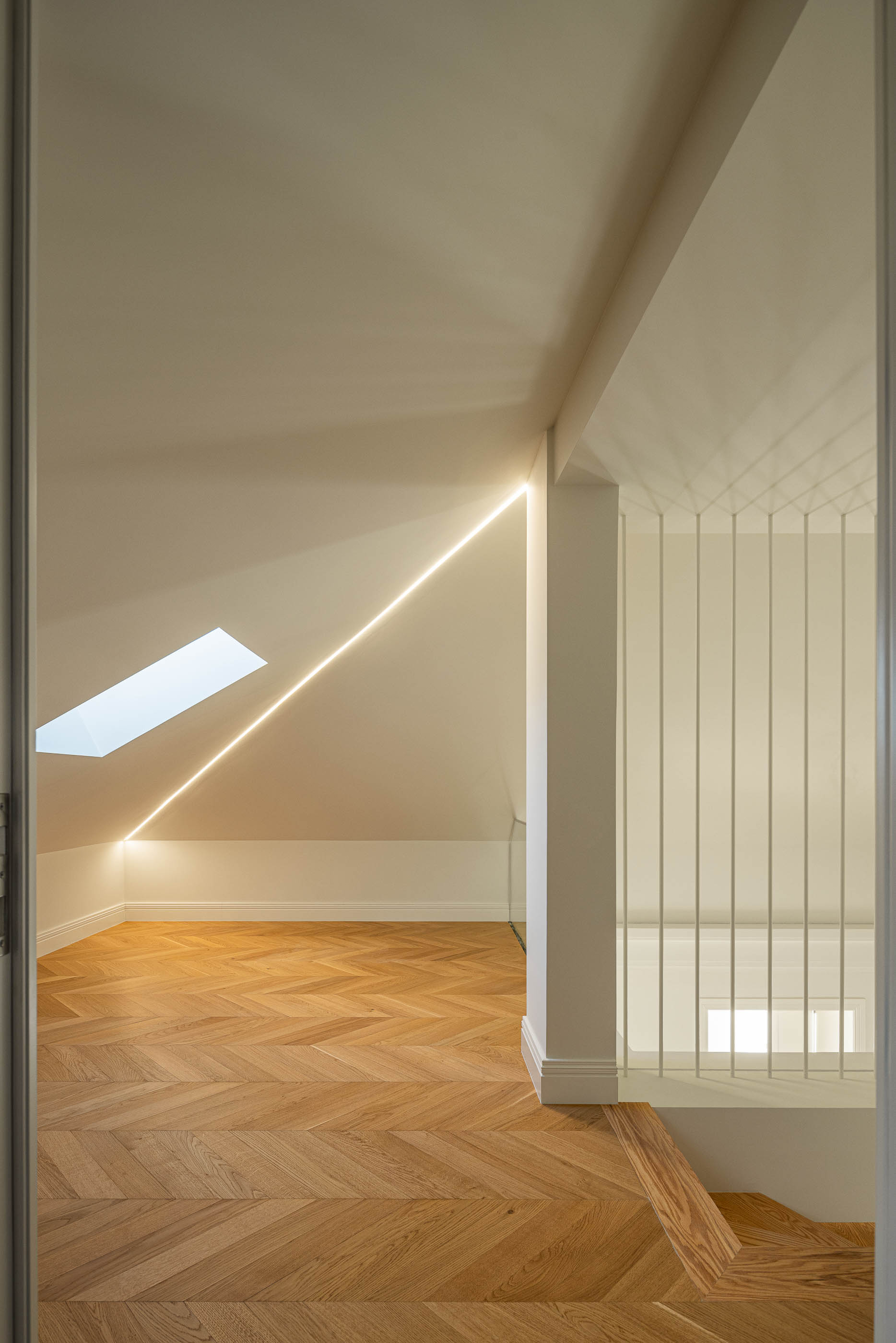 Sótão: Pavimento em madeira espinha de peixe, claraboia e iluminação linear embutida. — Condomínio das Artes arquitetura MiMool Arquitectura & Interiores em Porto