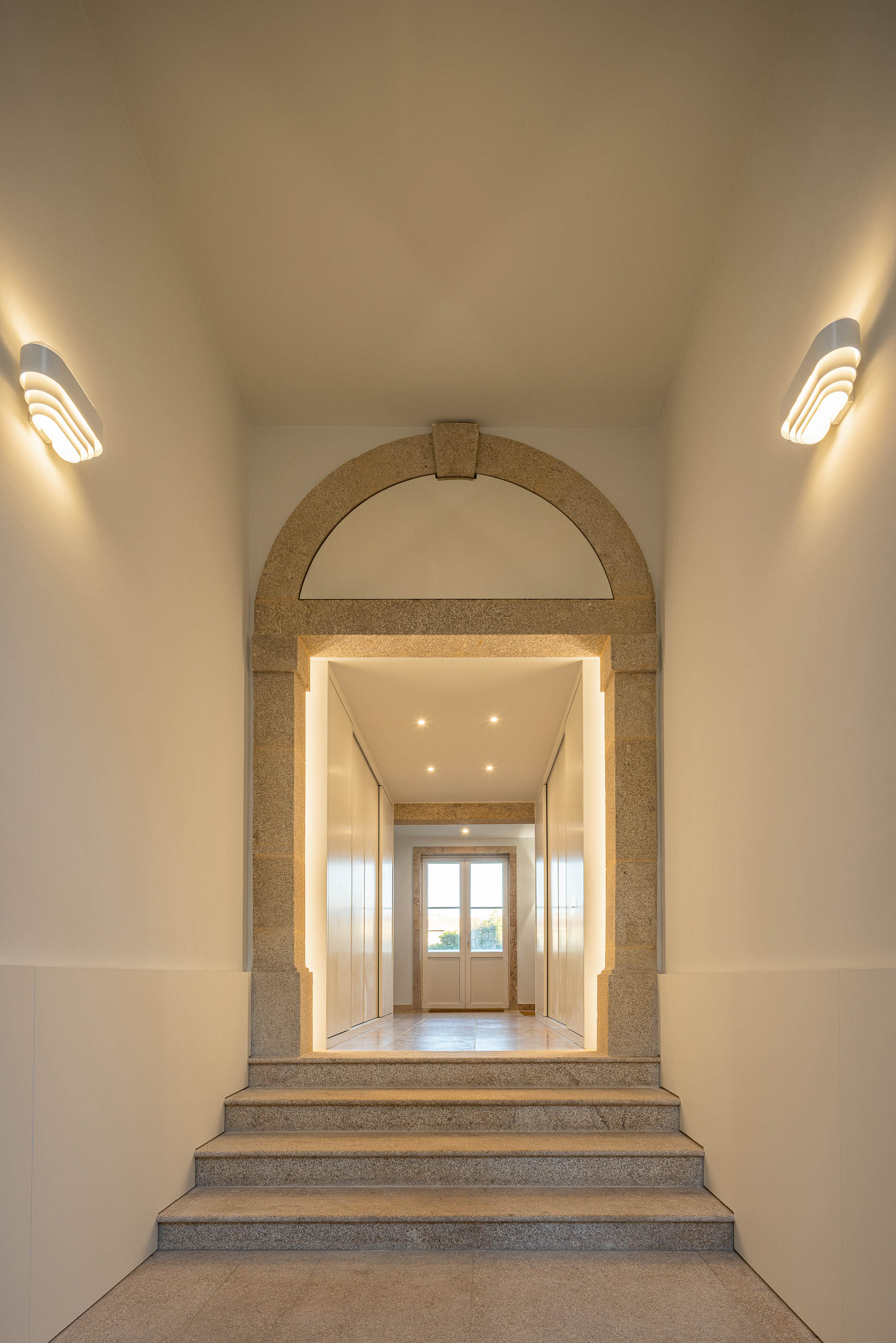 Hall de entrada: Arco em pedra rústica, pavimento em mosaico e candeeiros de parede modernos. — Condomínio das Artes arquitetura MiMool Arquitectura & Interiores em Porto
