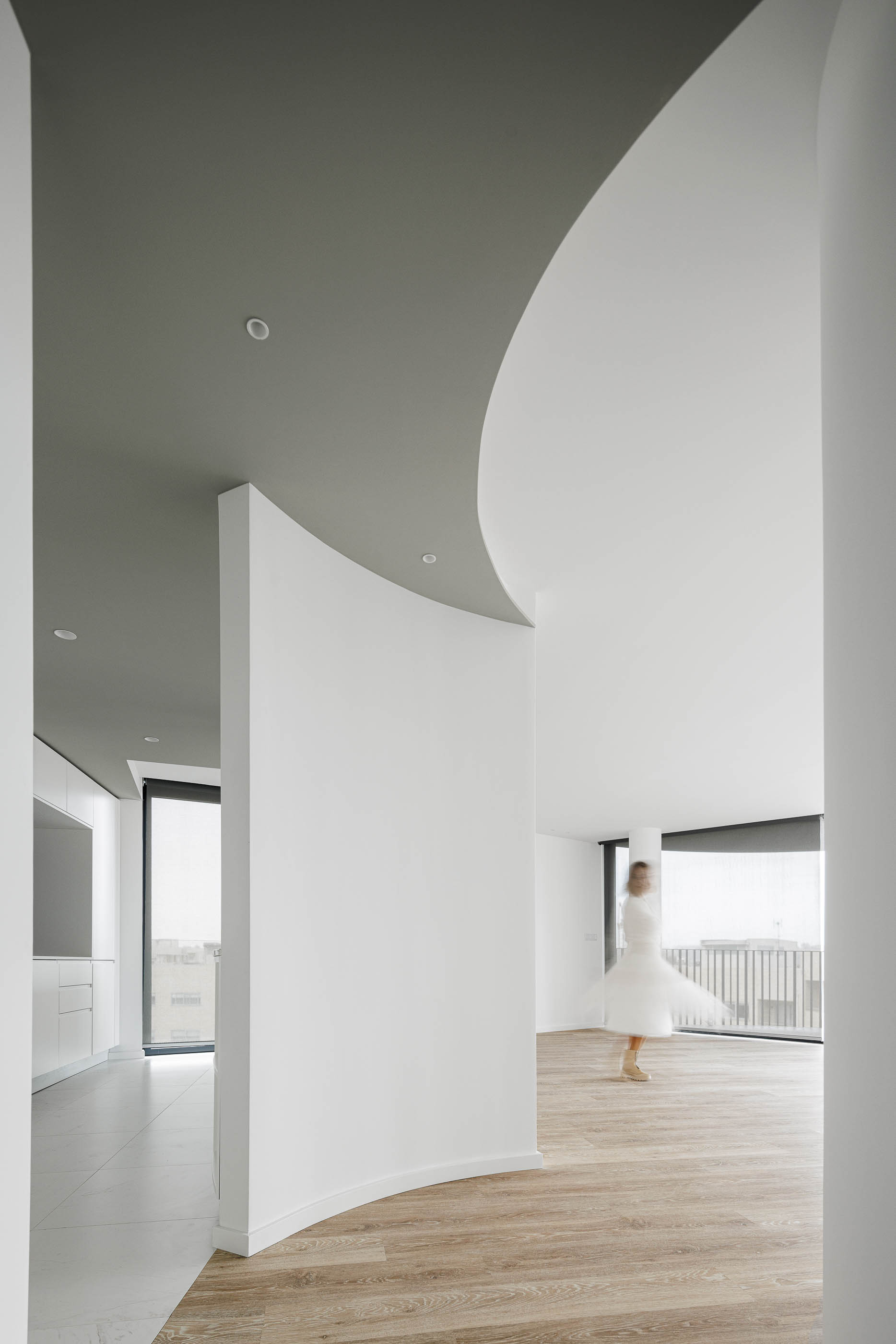 Hall de entrada: Espaço amplo com pavimento em madeira e cerâmica, paredes brancas curvas e iluminação embutida. — Edifício Sense 100 arquitetura Sandra Micaela Casinha Atelier em Rio Tinto