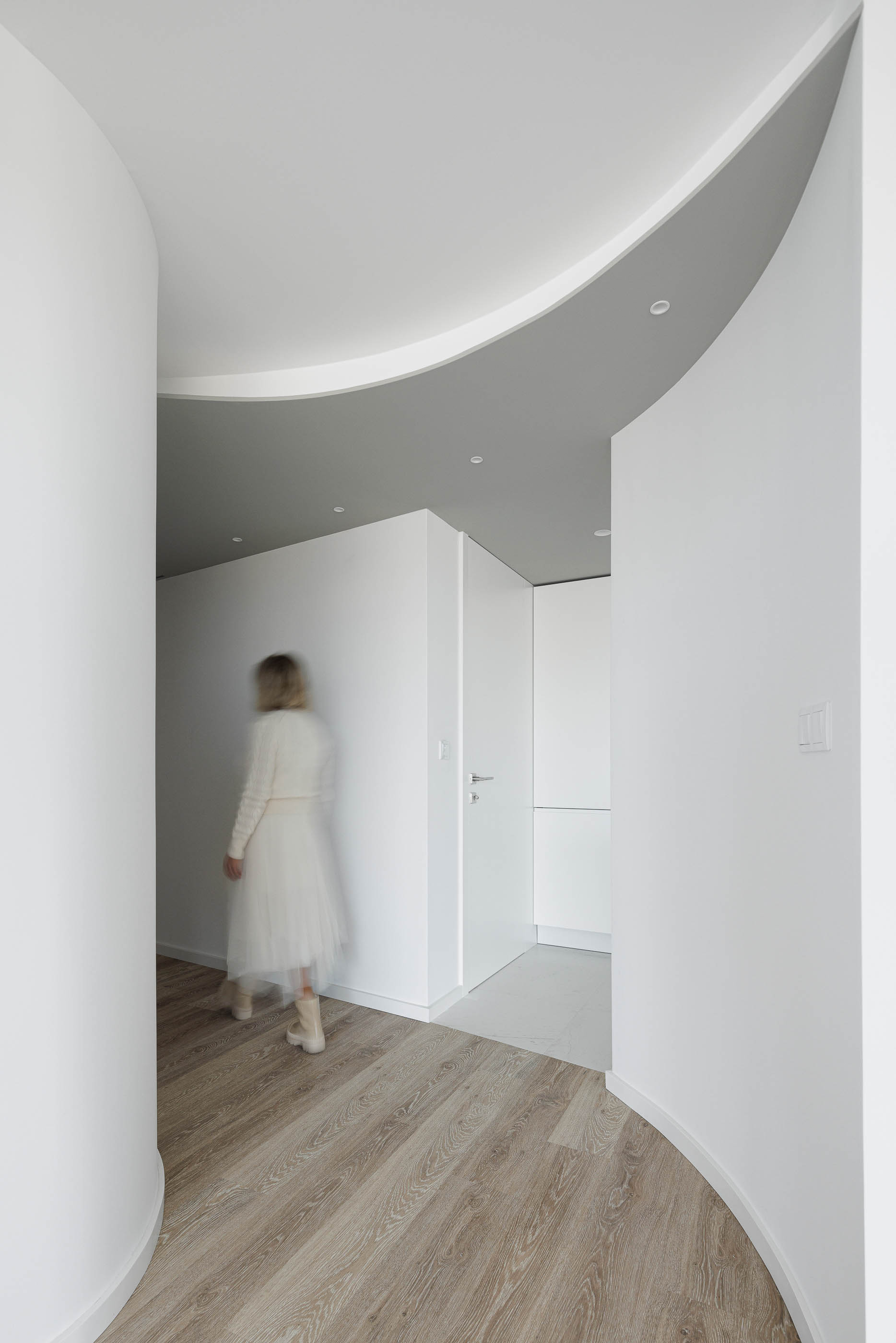 Hall de entrada: Corredor com paredes curvas brancas, pavimento em madeira e acesso a divisões com pavimento cerâmico. — Edifício Sense 100 arquitetura Sandra Micaela Casinha Atelier em Rio Tinto