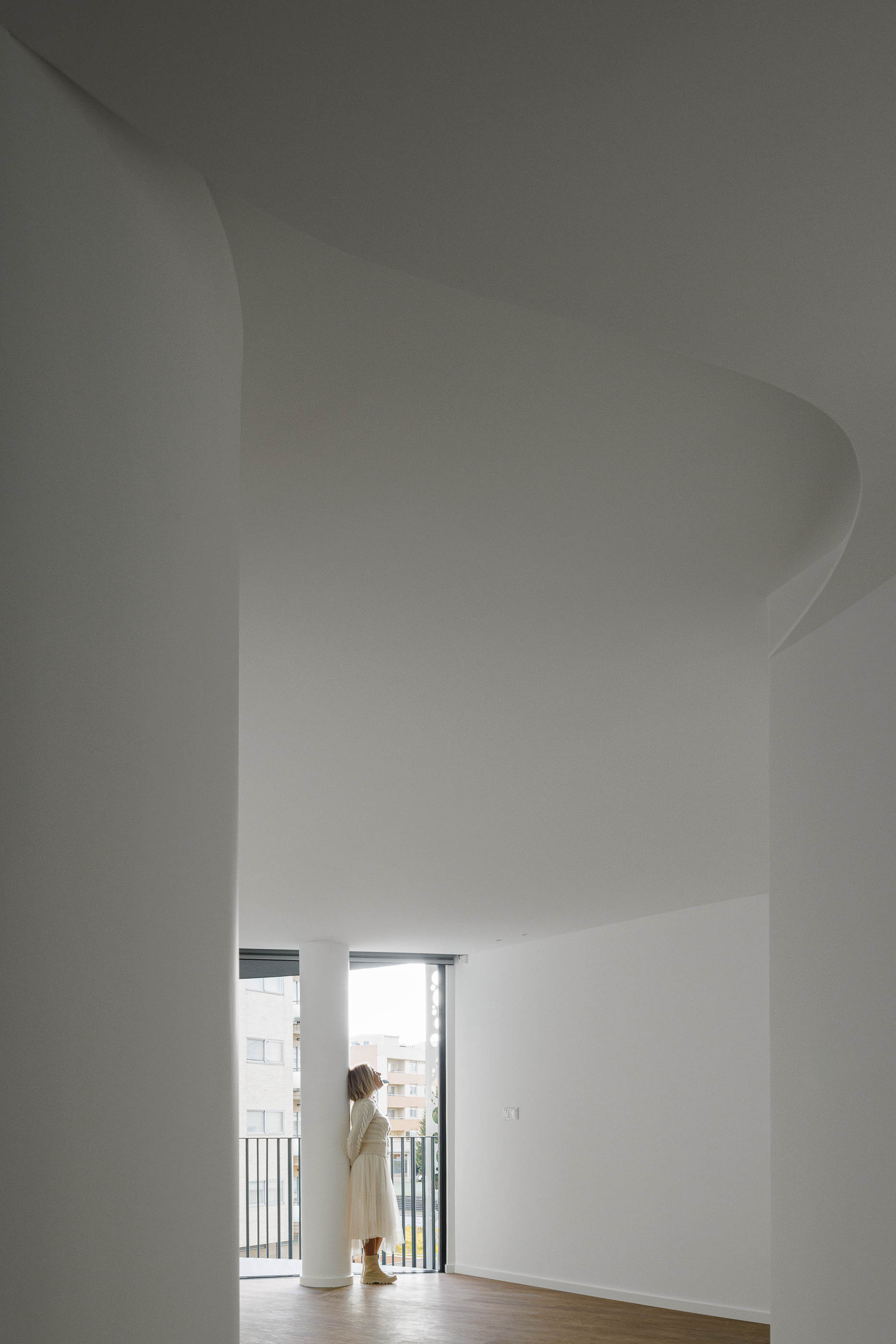 Hall de entrada: Corredor com paredes curvas brancas, pavimento em madeira e acesso à varanda. — Edifício Sense 100 arquitetura Sandra Micaela Casinha Atelier em Rio Tinto