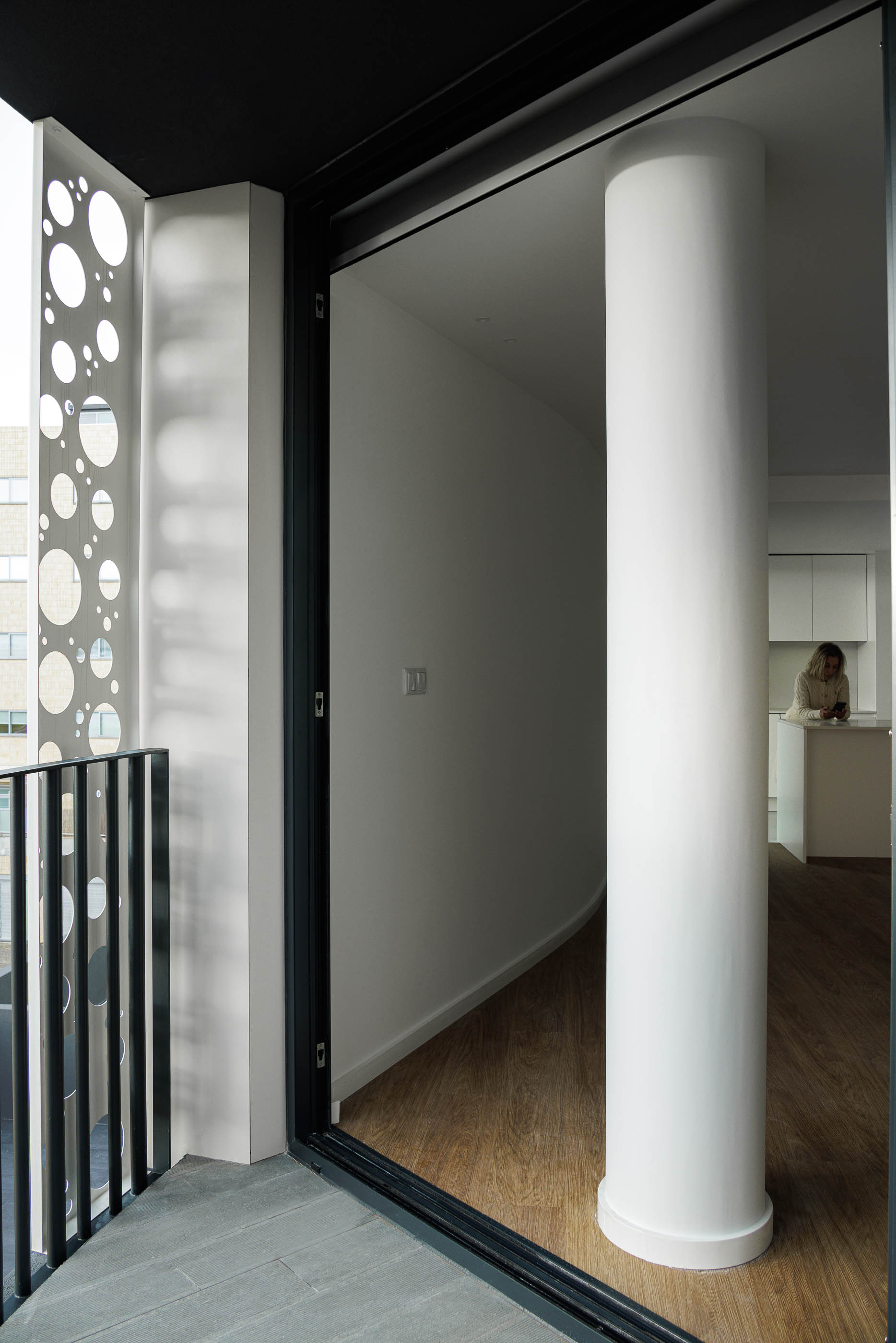 Varanda: Vista da varanda para o interior, mostrando a coluna circular e o acesso à cozinha. — Edifício Sense 100 arquitetura Sandra Micaela Casinha Atelier em Rio Tinto