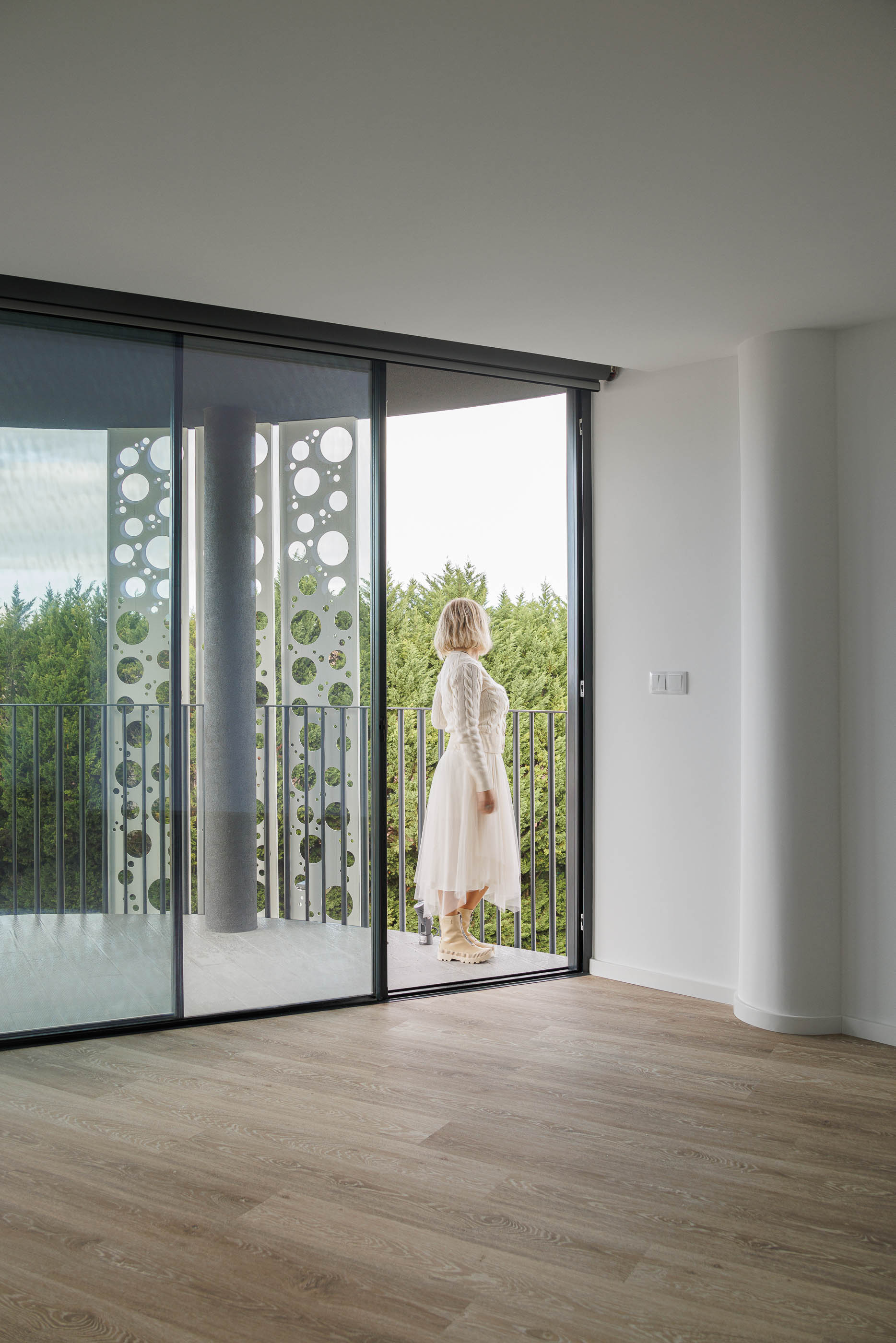 Varanda: Vista da varanda com pavimento em madeira, guarda-corpo em metal preto e vista para a vegetação. — Edifício Sense 100 arquitetura Sandra Micaela Casinha Atelier em Rio Tinto