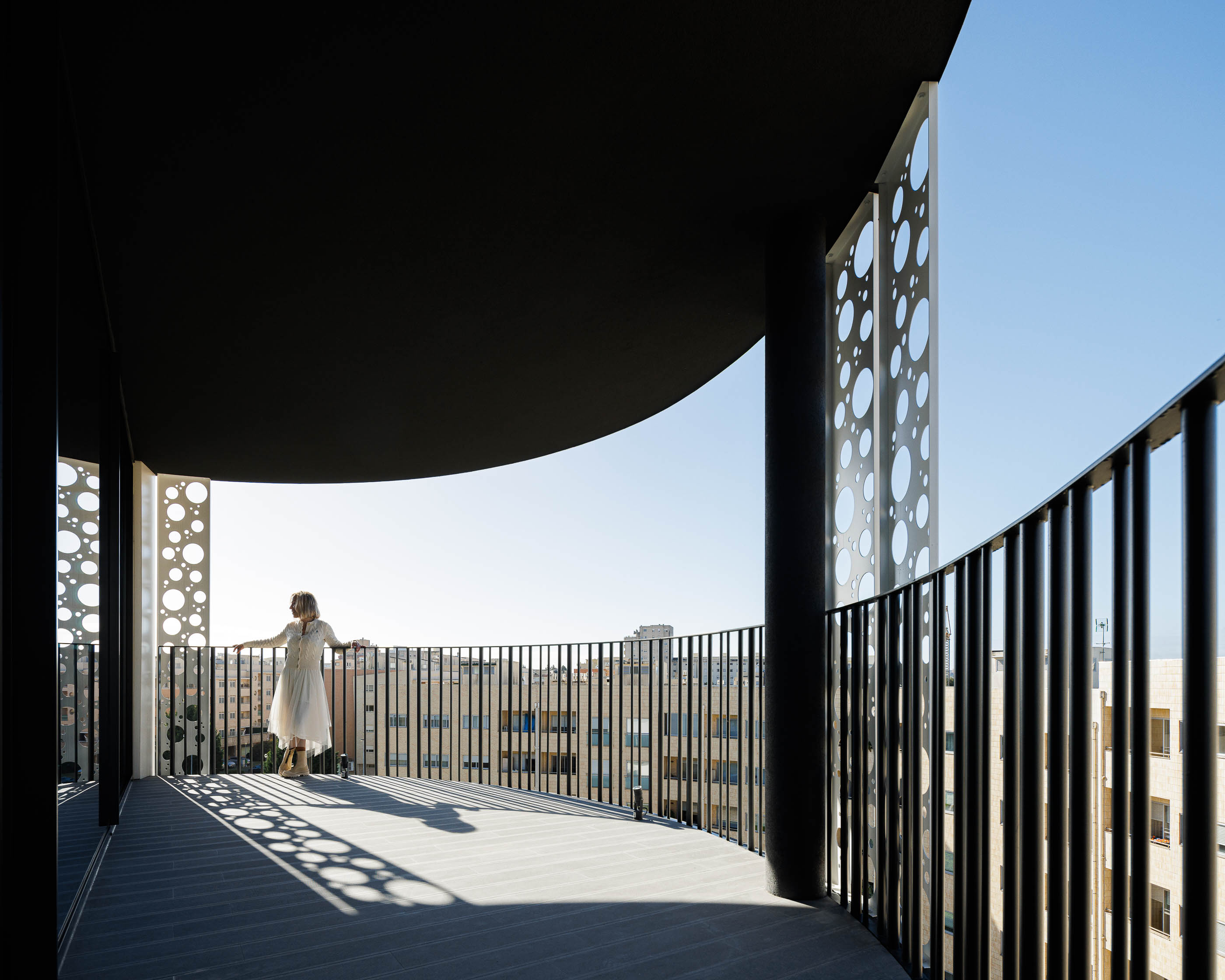 Varanda: Vista da varanda com pavimento em madeira, guarda-corpo em metal preto e vista para a cidade. — Edifício Sense 100 arquitetura Sandra Micaela Casinha Atelier em Rio Tinto