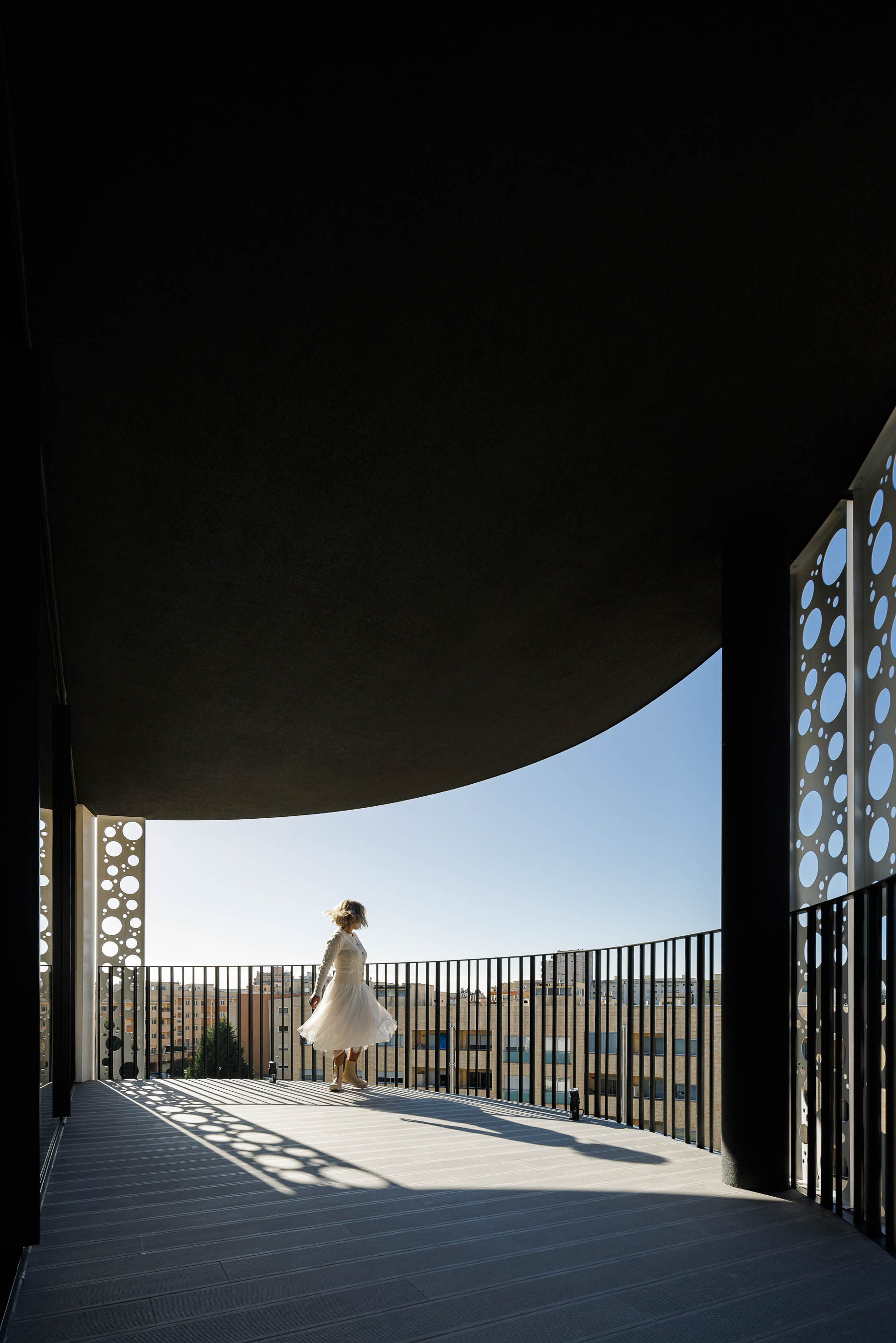 Varanda: Vista da varanda com pavimento em madeira, guarda-corpo em metal preto e vista para a cidade. — Edifício Sense 100 arquitetura Sandra Micaela Casinha Atelier em Rio Tinto