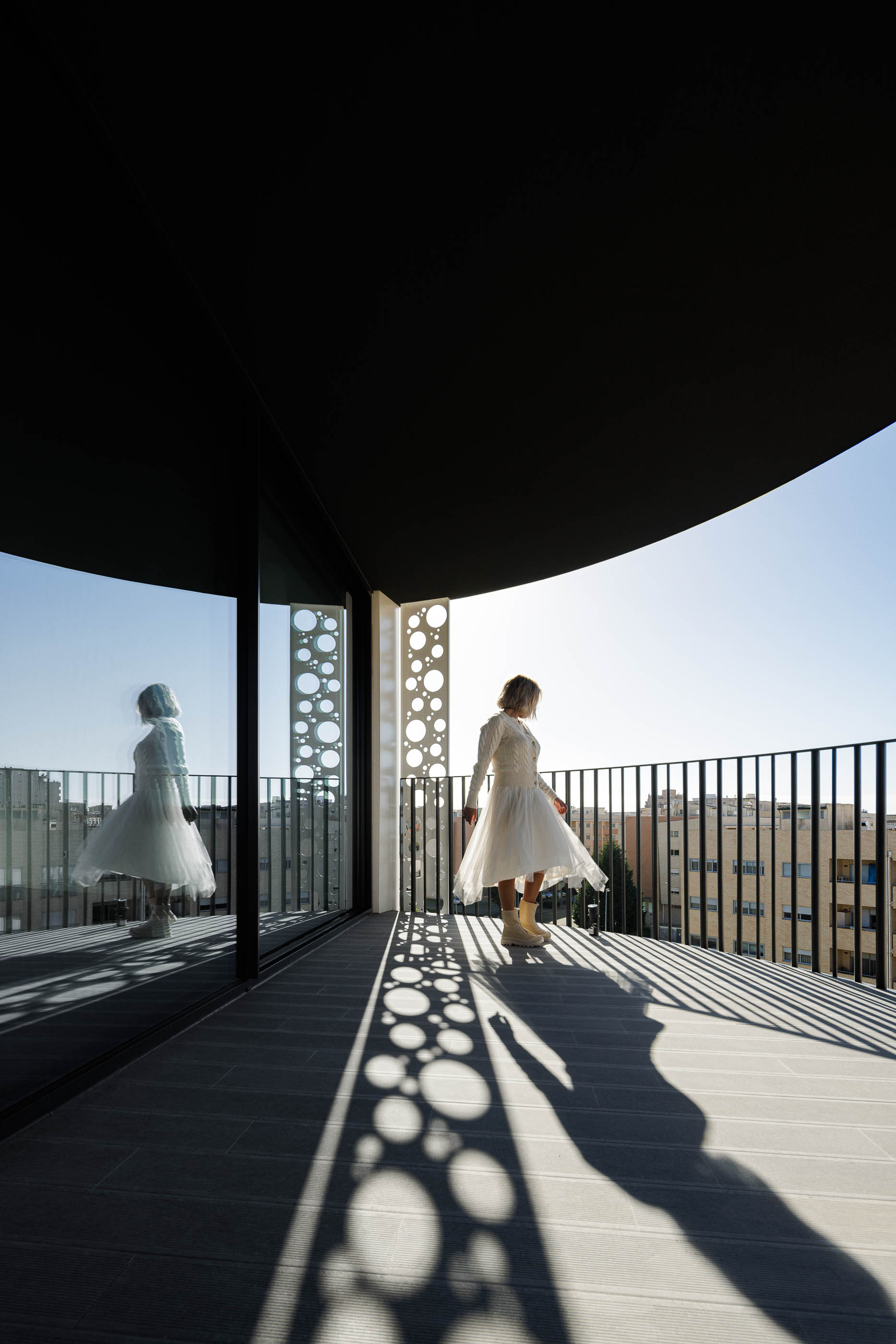 Varanda: Reflexo da varanda no vidro, com pavimento em madeira e guarda-corpo em metal preto. — Edifício Sense 100 arquitetura Sandra Micaela Casinha Atelier em Rio Tinto