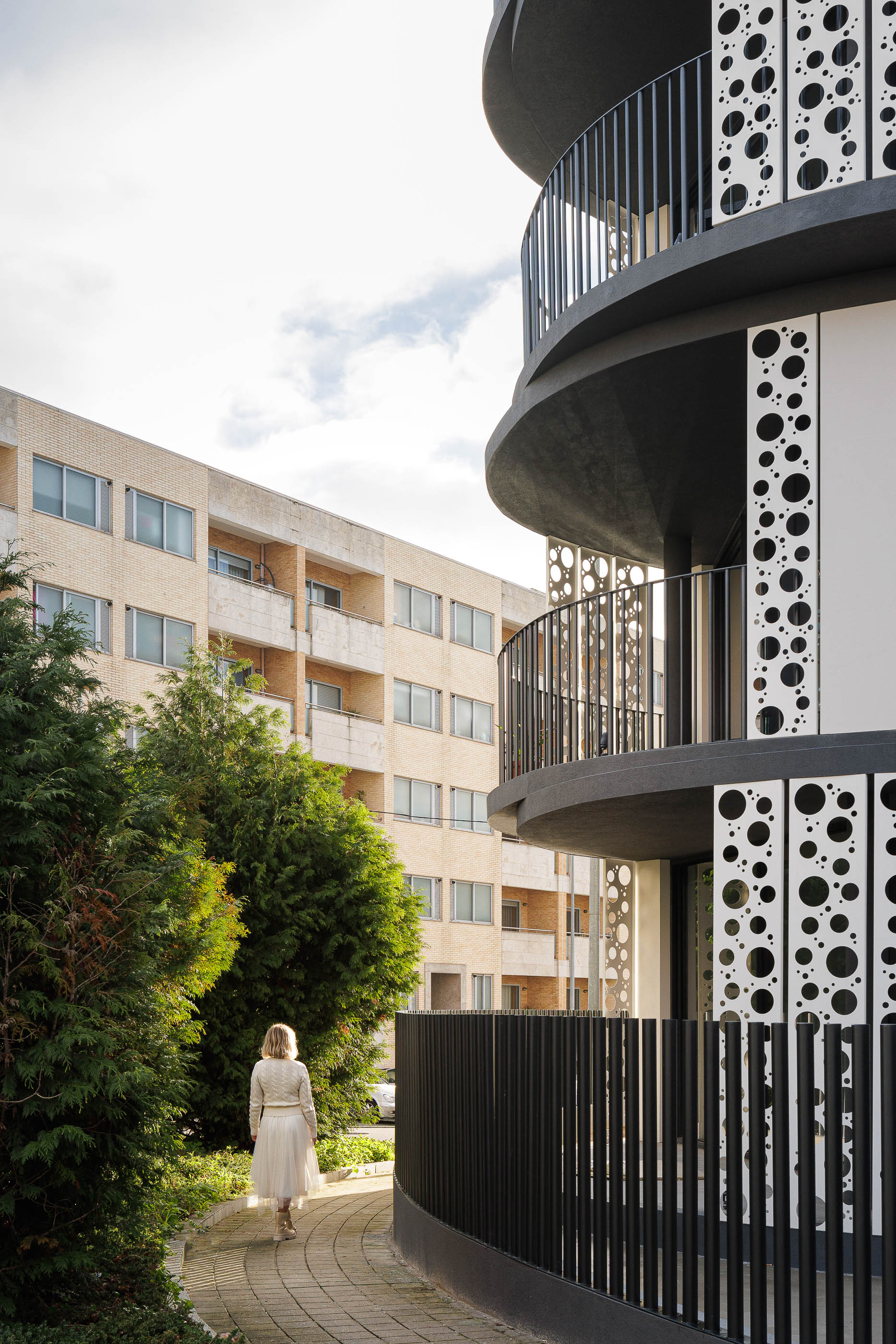 Exterior: Edifício com varandas curvas e elementos decorativos circulares, integrado na paisagem urbana. — Edifício Sense 100 arquitetura Sandra Micaela Casinha Atelier em Rio Tinto