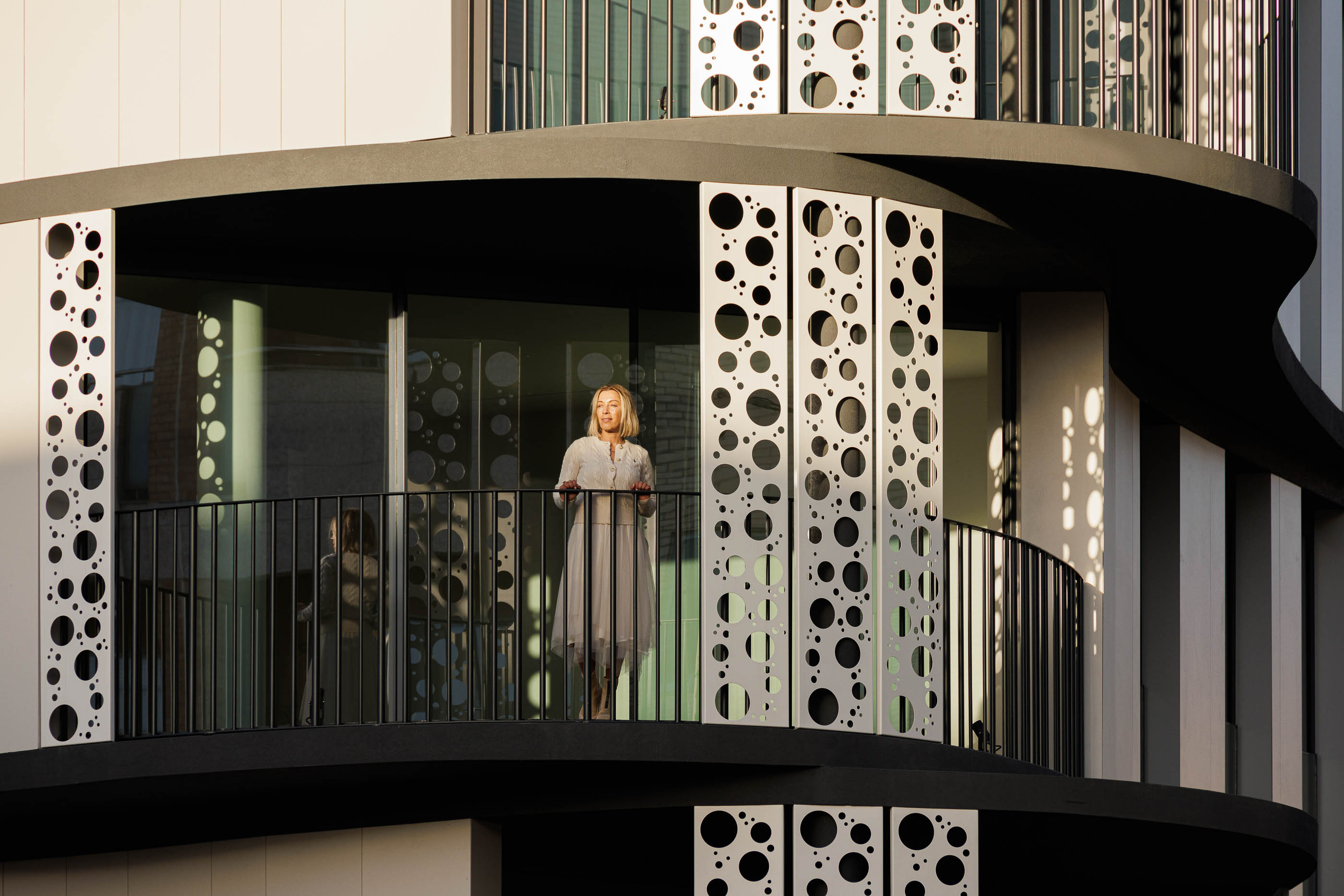 Varanda: Vista da varanda com pavimento em madeira, guarda-corpo em metal preto e estrutura perfurada. — Edifício Sense 100 arquitetura Sandra Micaela Casinha Atelier em Rio Tinto