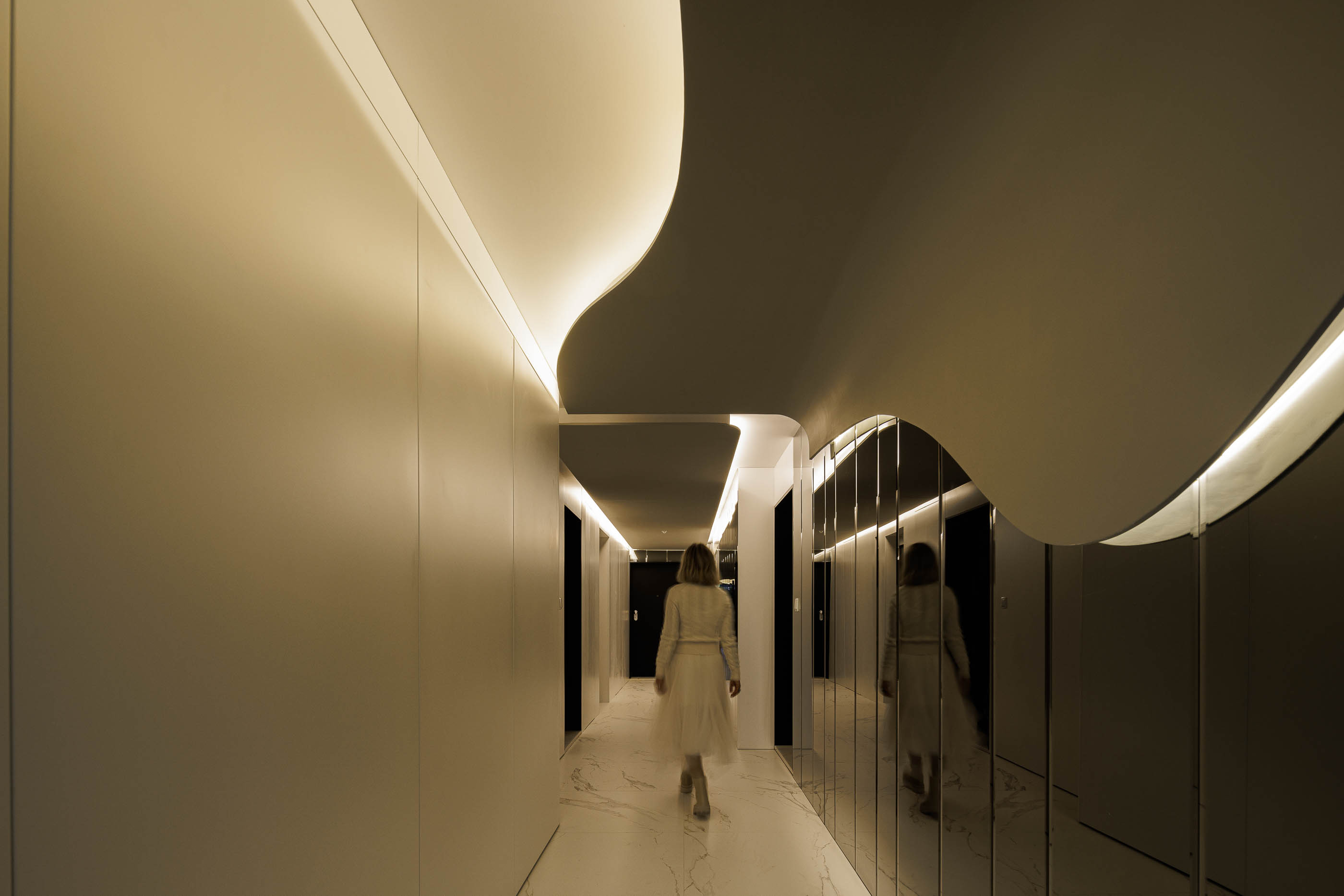 Corredor: Espaço com paredes brancas curvas, espelhos e pavimento em mármore branco. — Edifício Sense 100 arquitetura Sandra Micaela Casinha Atelier em Rio Tinto