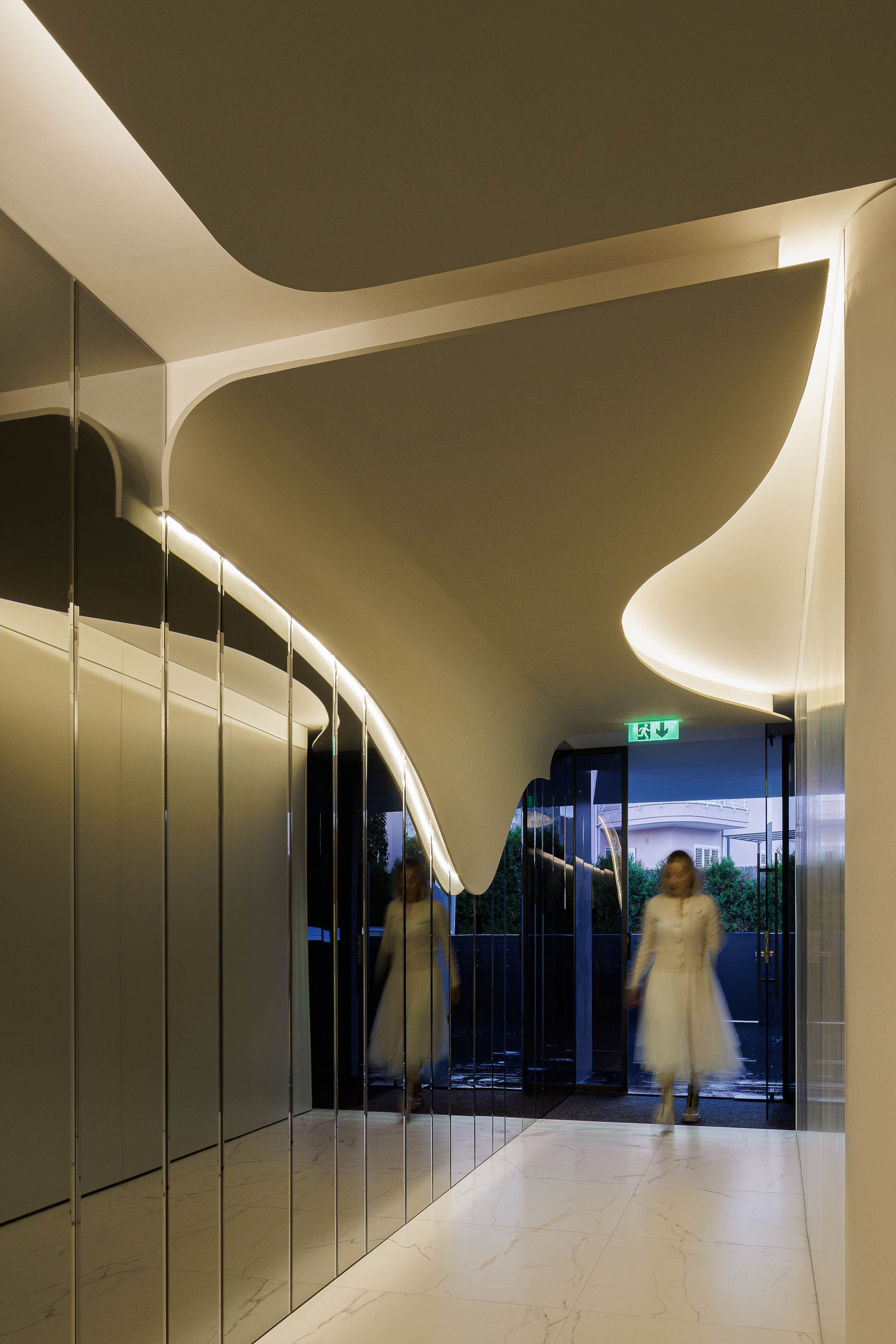 Corredor: Espaço com paredes brancas curvas, espelhos e pavimento em mármore branco, com iluminação embutida. — Edifício Sense 100 arquitetura Sandra Micaela Casinha Atelier em Rio Tinto