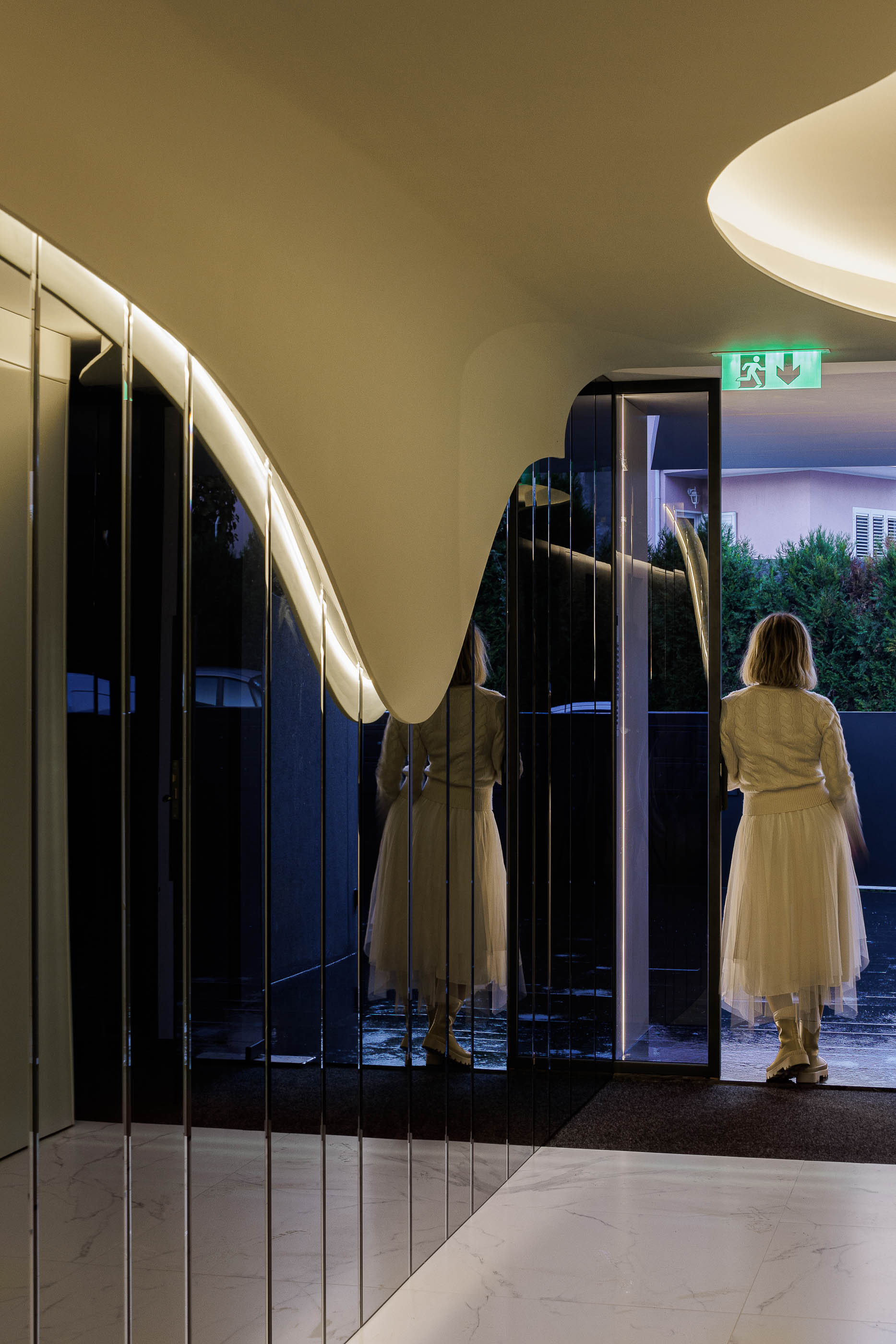 Corredor: Espaço com paredes brancas curvas, espelhos e pavimento em mármore branco, com porta de saída. — Edifício Sense 100 arquitetura Sandra Micaela Casinha Atelier em Rio Tinto